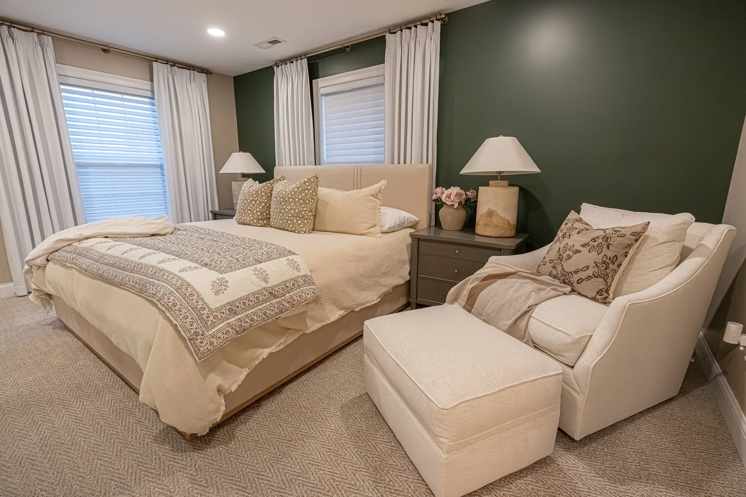 Guest bedroom with a green accent wall, warm neutral bedding, symmetrical nightstands and lamps, and an upholstered chaise in an Oakwood, Ohio home