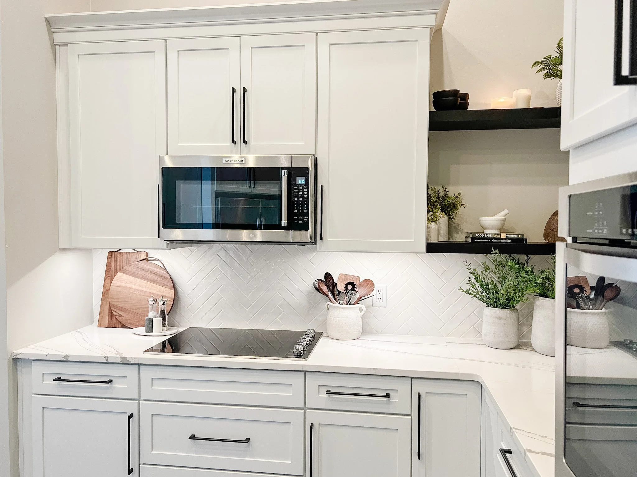 White kitchen detail with a cooktop, stainless microwave, marble-look countertop, and a styled floating wood shelf in a Centerville, Ohio renovation