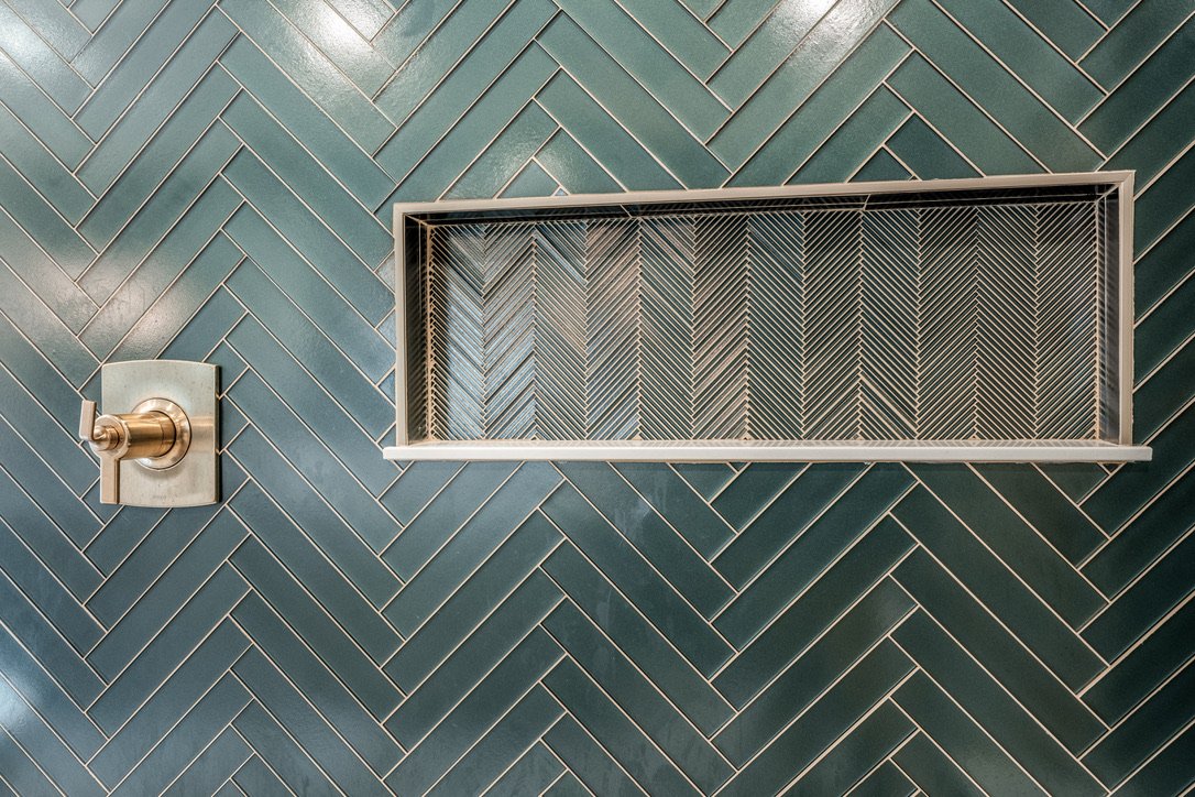 Detail of matte green glass herringbone tile with a custom recessed shower niche and gold trim in a Xenia, Ohio spa bathroom