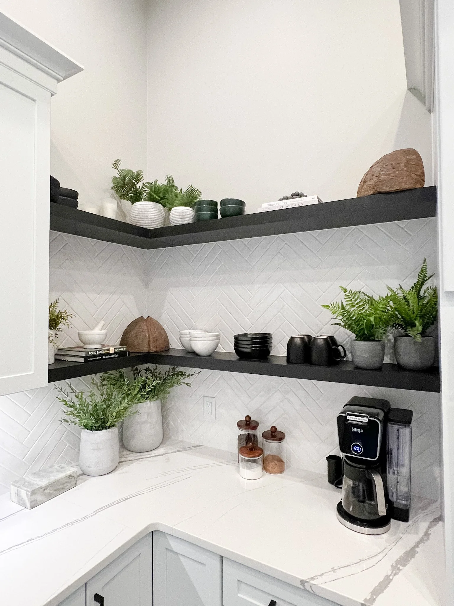 White herringbone tile backsplash with dark floating shelves styled with greenery and dishware in a Centerville, Ohio kitchen