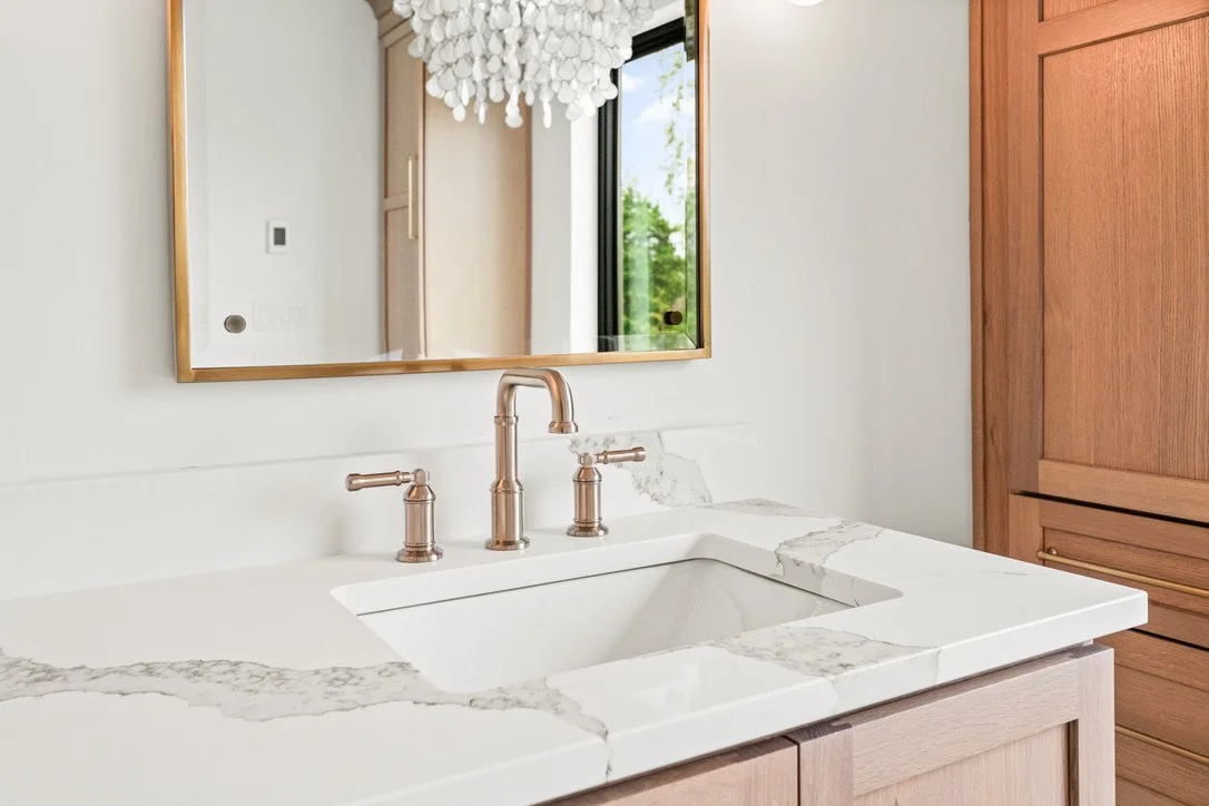 Bathroom vanity with a white sink, brass widespread faucet, and marble countertop beneath a gold-framed mirror in a Brookville, Ohio master bathroom.
