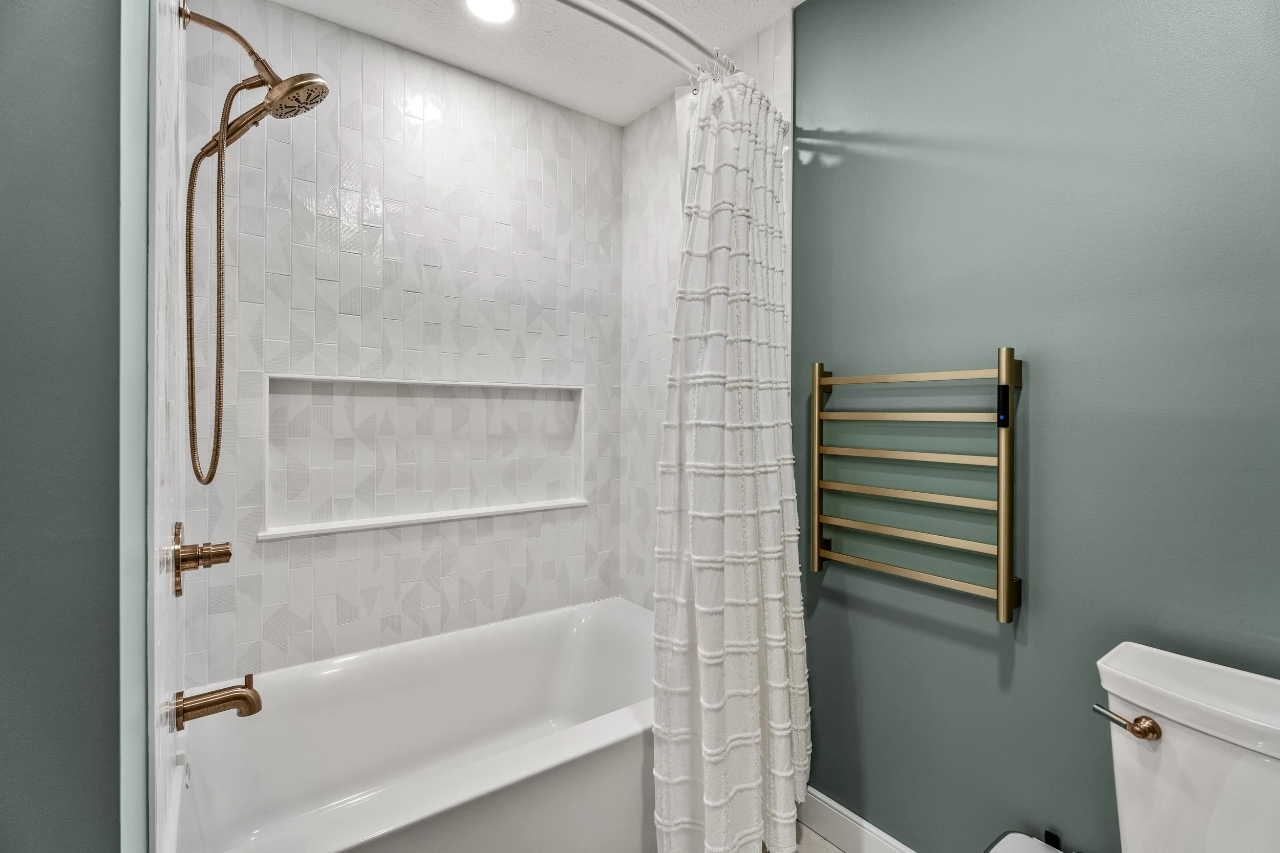 Basement bathroom shower in Centerville, Ohio with custom tile, shampoo niche, gold fixtures, and tub by White Oak Interiors