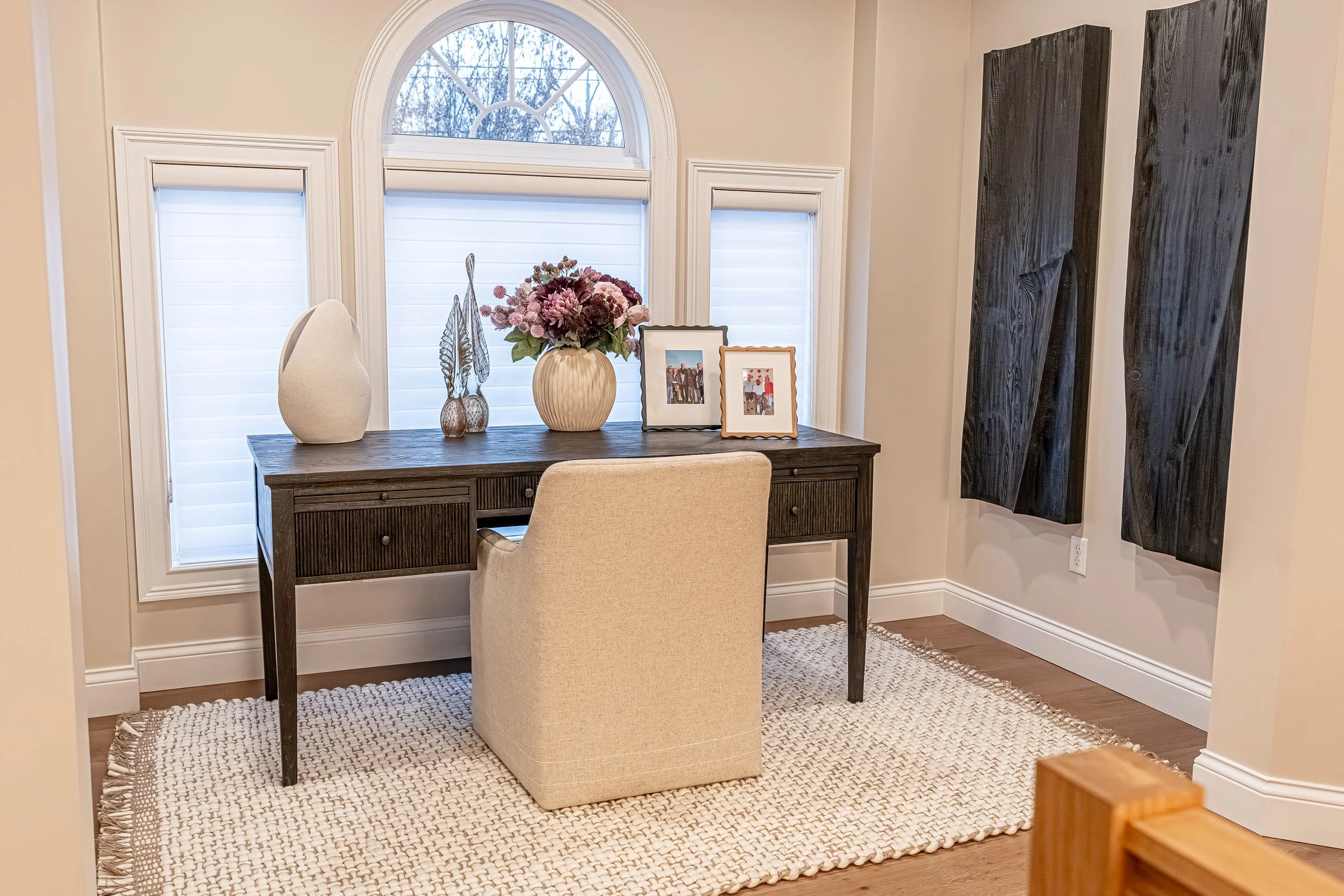 Cozy office loft with a black reeded desk beneath arched windows, layered natural light, and a large dimensional wood art piece in an Oakwood, Ohio renovation