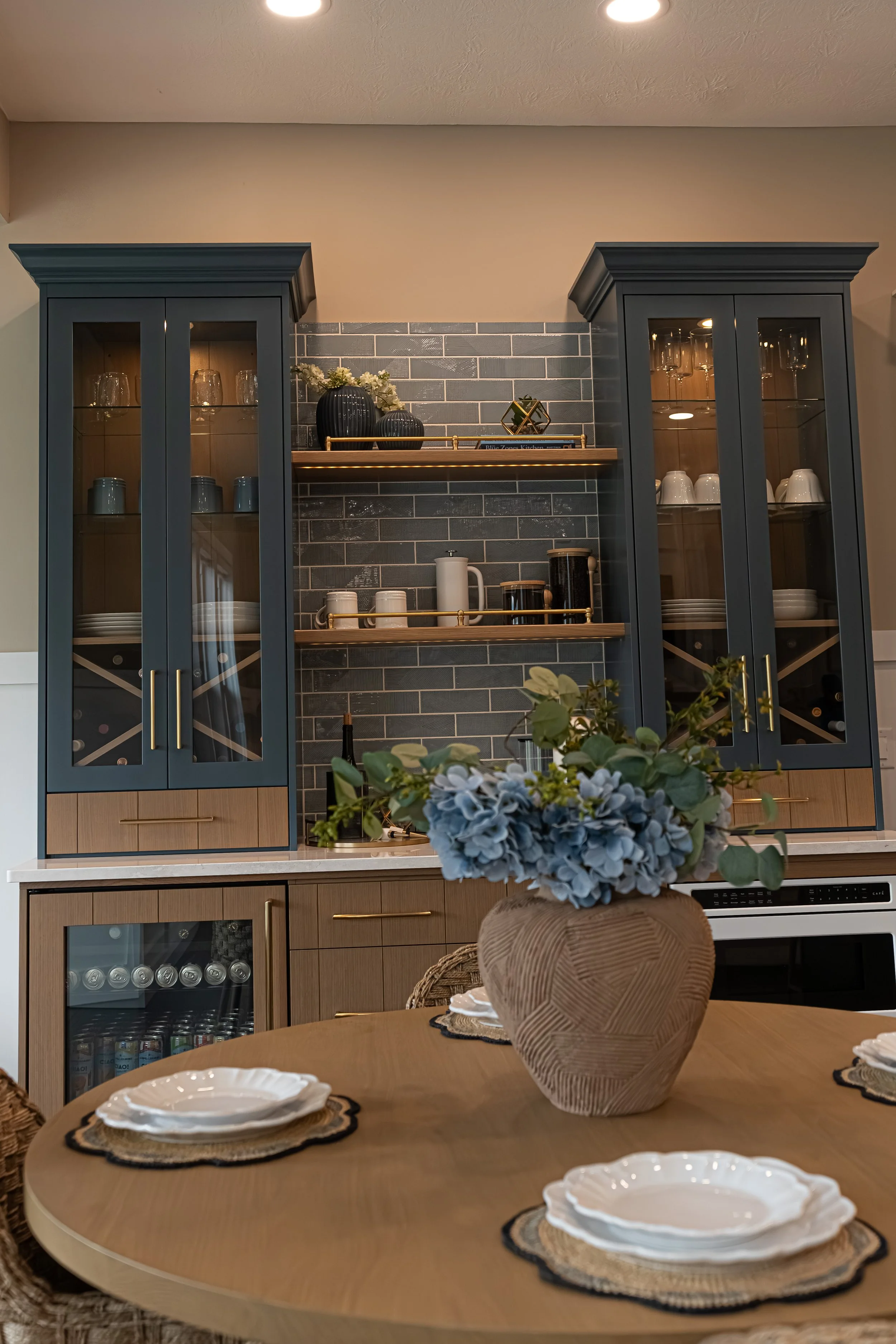 Built-in coffee bar with navy glass-front cabinets, gray subway tile, open wood shelving, and a beverage fridge in a Centerville home renovation.