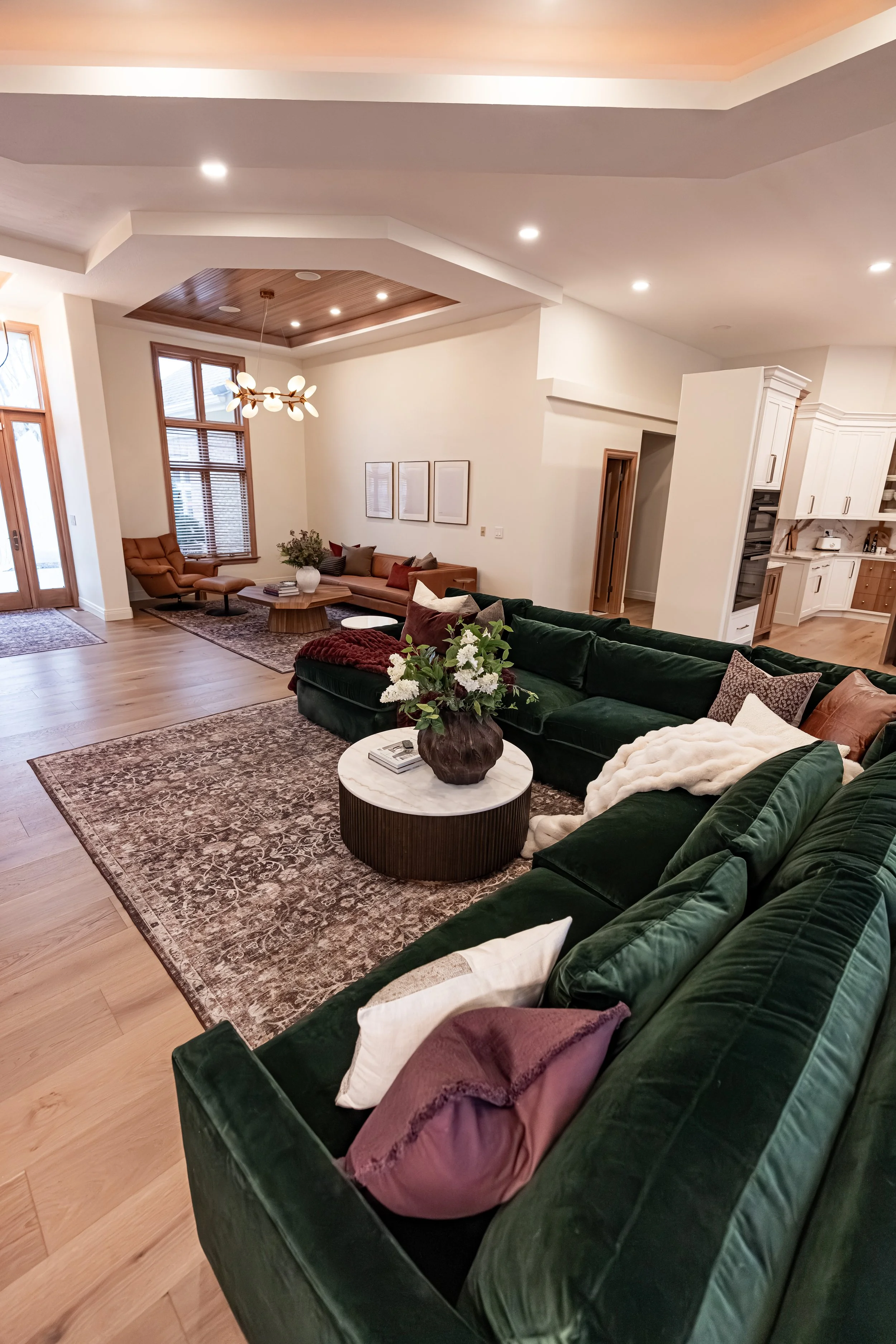 Open-concept Bellbrook, Ohio living area with green velvet sectional, wood tray ceiling, and second sitting area off the kitchen