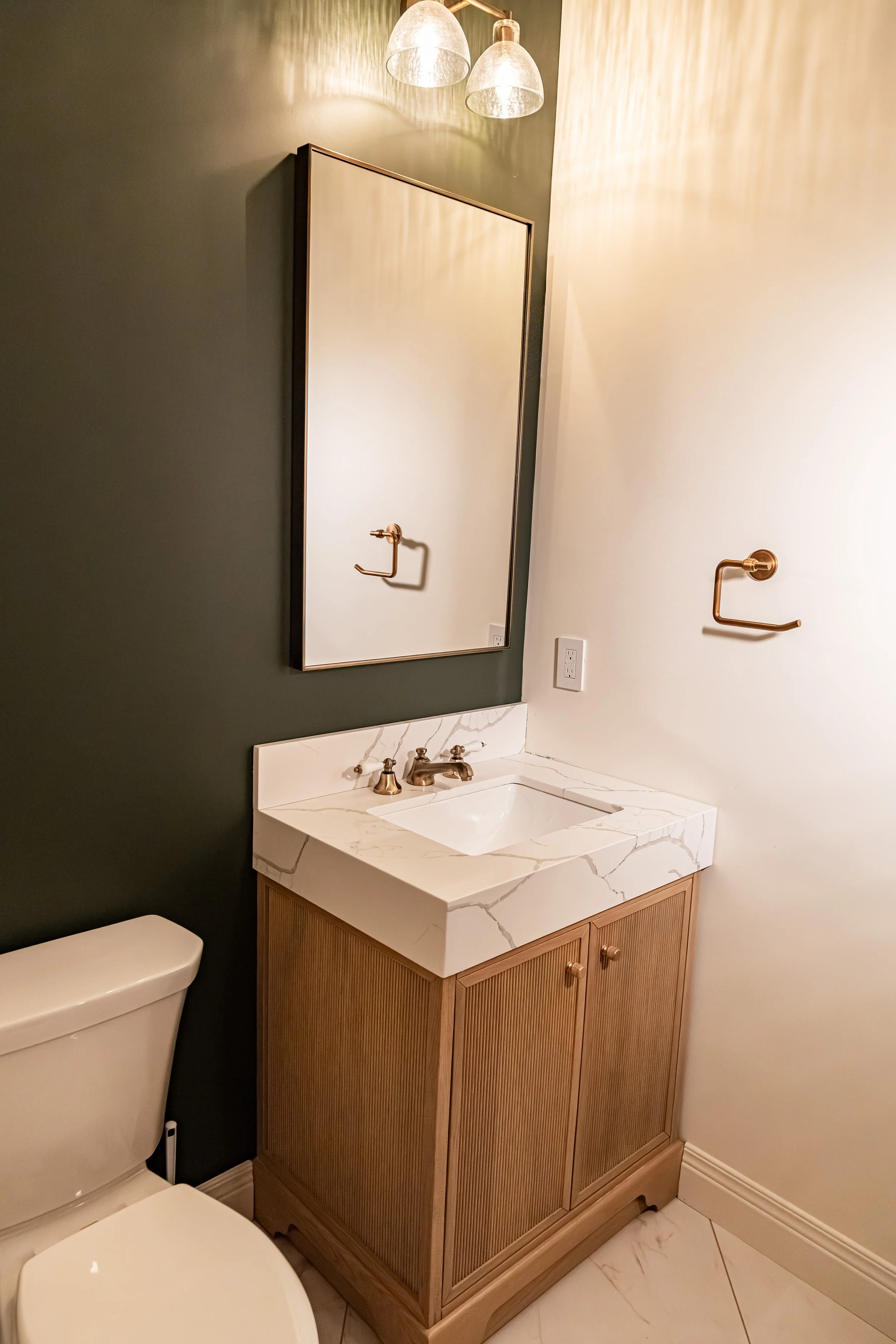 Powder room with deep green walls, a wood vanity with marble countertop, and aged-brass fixtures in a Bellbrook whole-home remodel.