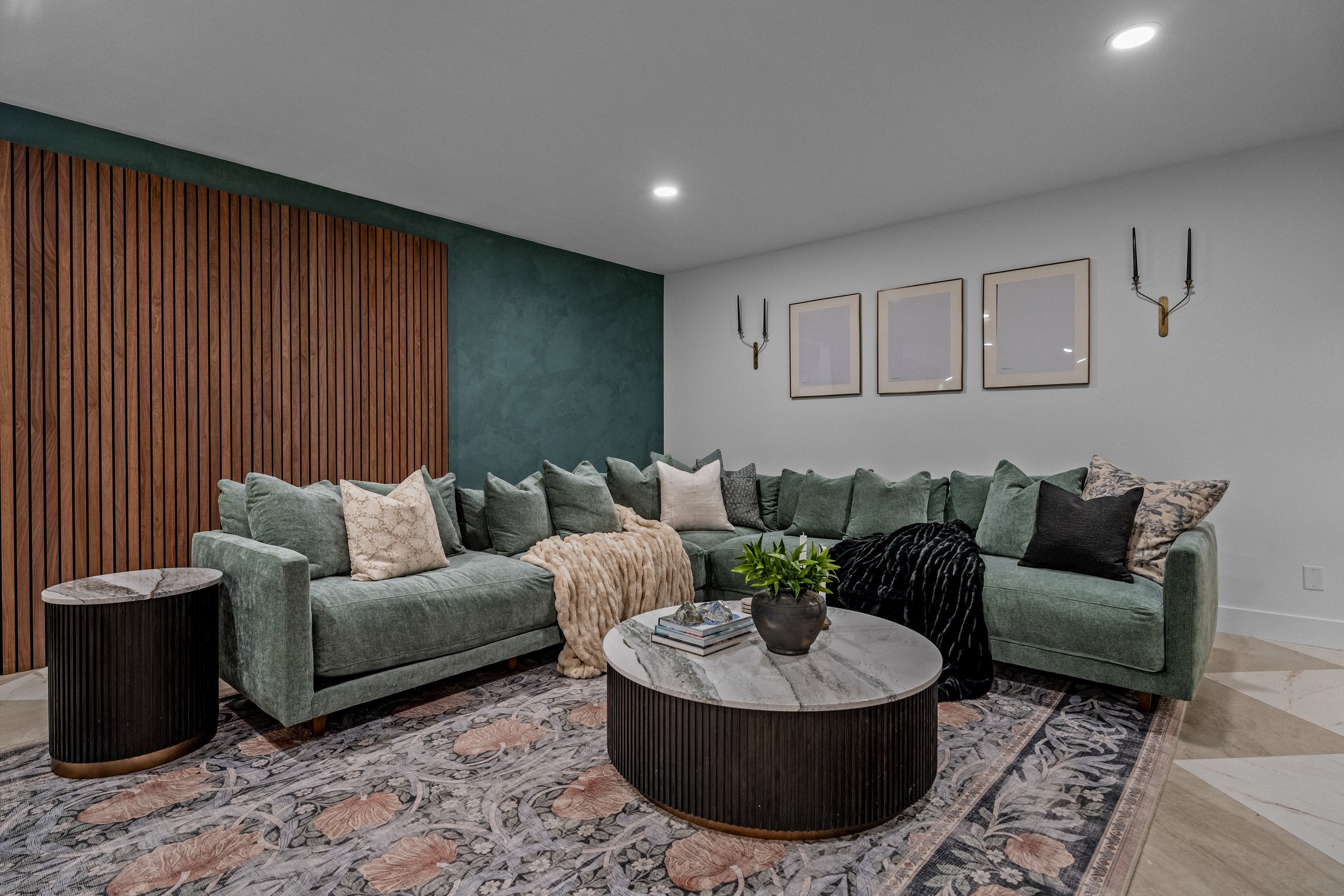 Finished basement living room in Centerville, Ohio with a green sectional, wood slat-wall feature, and styled coffee table by White Oak Interiors