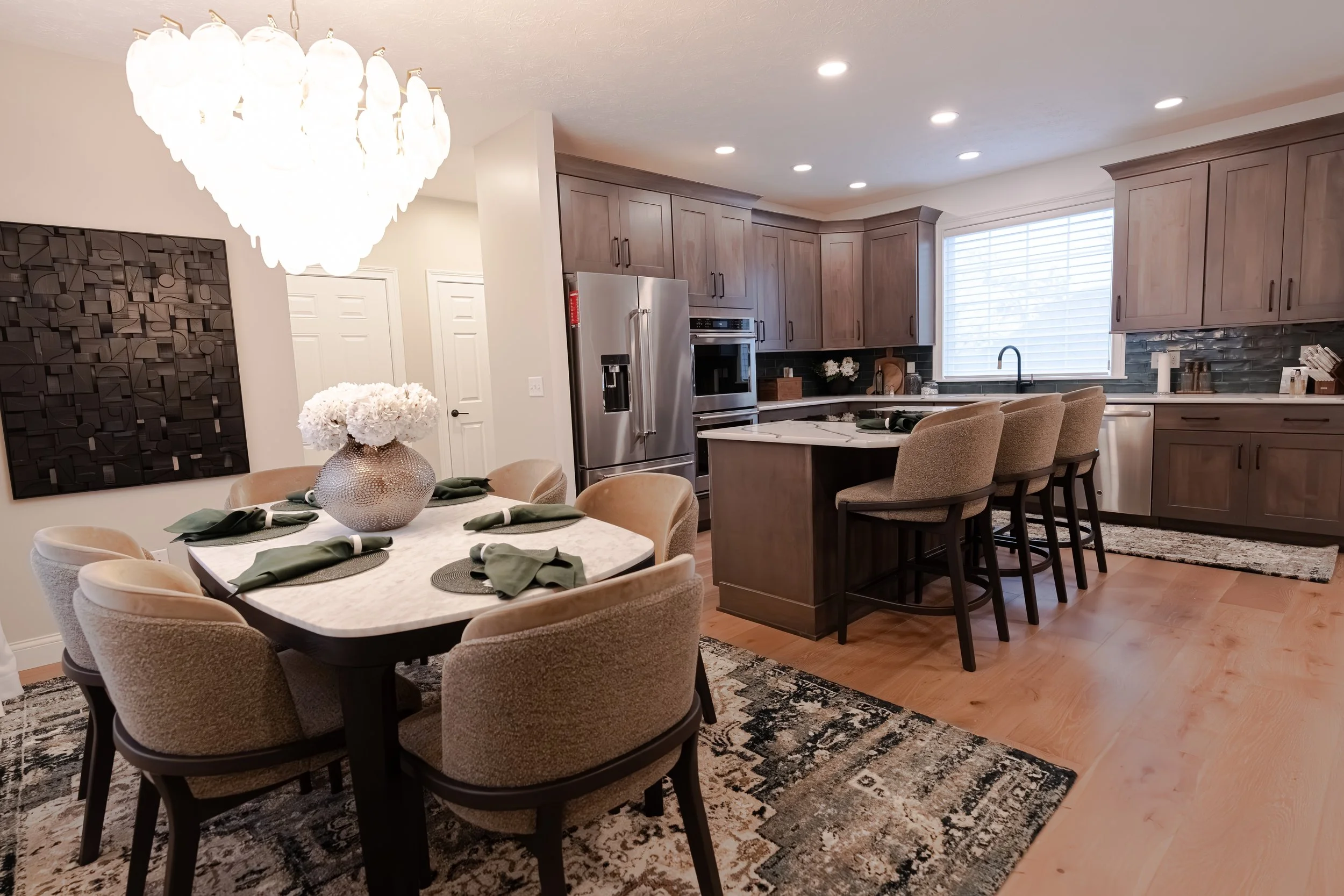Open-concept dining area with an upholstered table set, fogged-glass chandelier, and patterned rug, flowing into the kitchen with a center island in Oakwood, Ohio