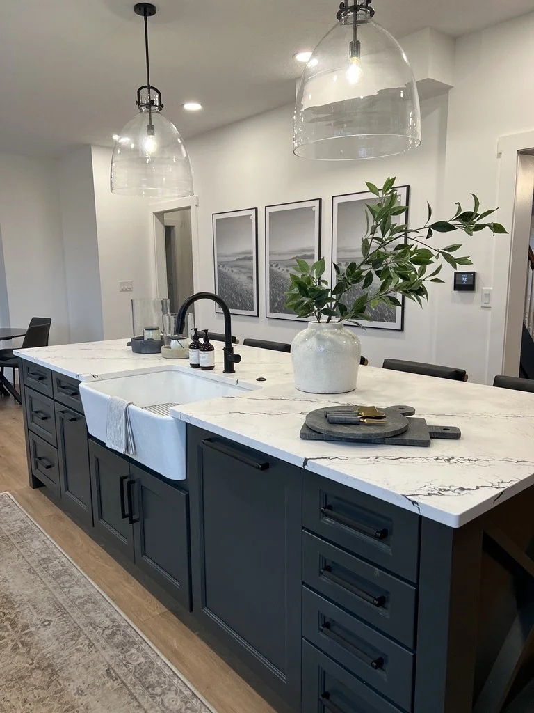 Green kitchen island with a double farmhouse apron-front sink, quartz countertop, black faucet, glass pendants, and a framed gallery wall in a Springboro, Ohio home
