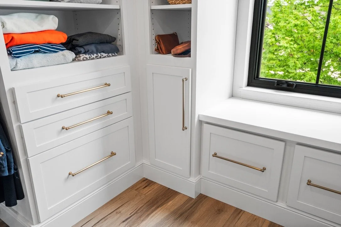 Closet built-ins with open cubbies and brass bar pulls beside a window in a Brookville, Ohio master suite.