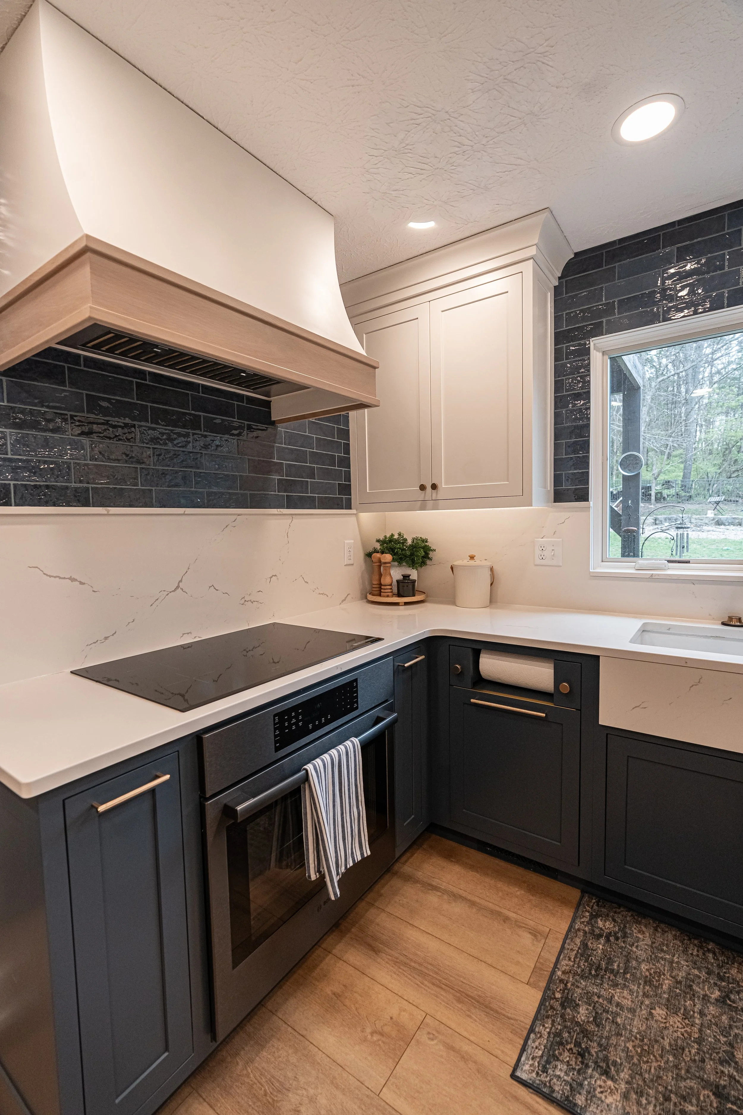 Kitchen cooktop wall with a wood range hood, dark subway tile backsplash, and navy cabinets in a Centerville whole-home remodel.
