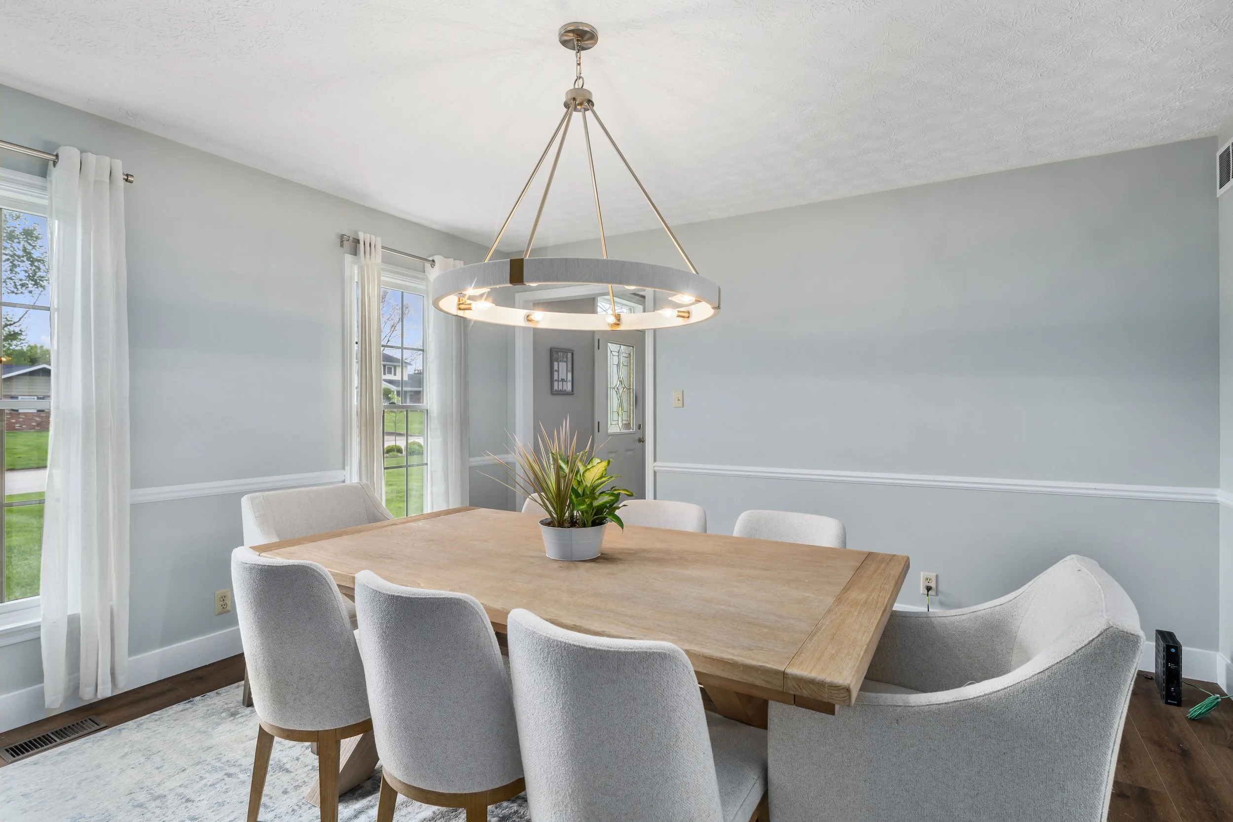 Renovated dining room with a wood table, upholstered chairs, soft blue-gray walls, and a round modern chandelier