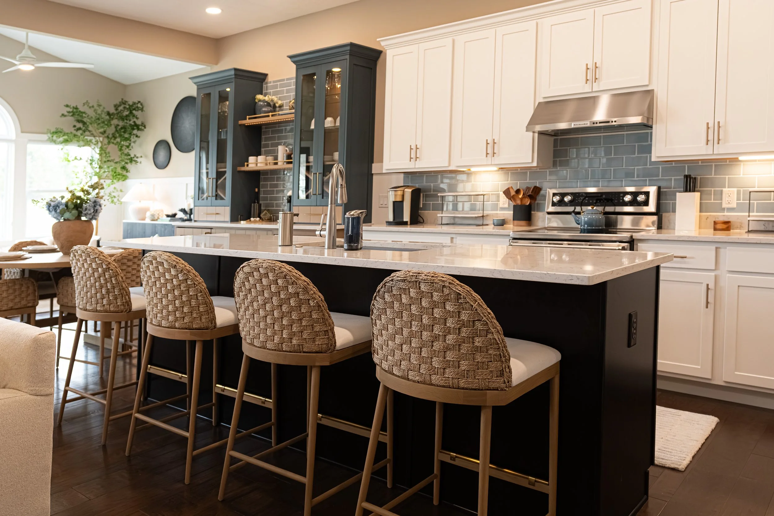 Kitchen island with a marble-look waterfall counter, woven stools, and white-and-navy cabinetry with gray subway tile in a Centerville home renovation.