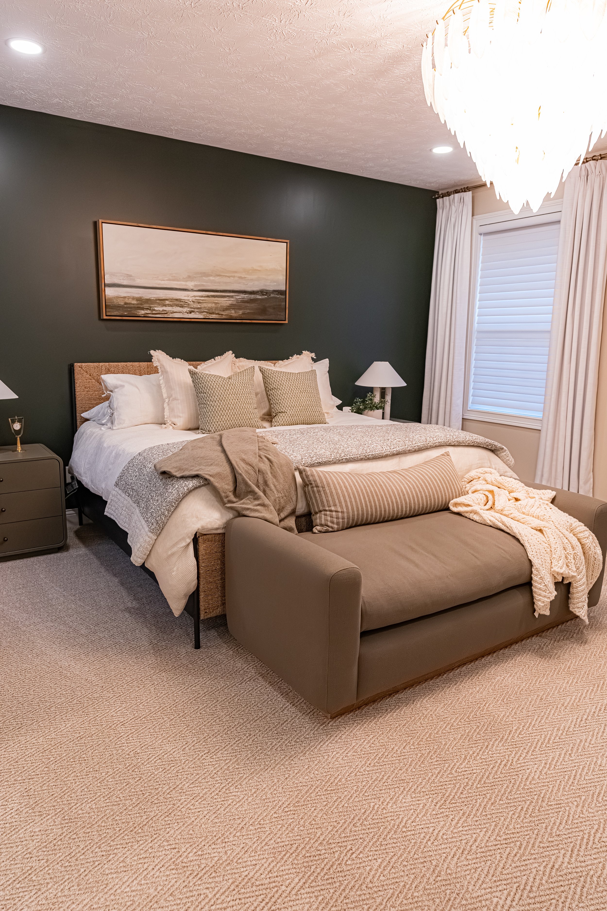 Master bedroom with a green accent wall, upholstered bed and chaise, layered neutral bedding, and a herringbone-patterned carpet in an Oakwood, Ohio home