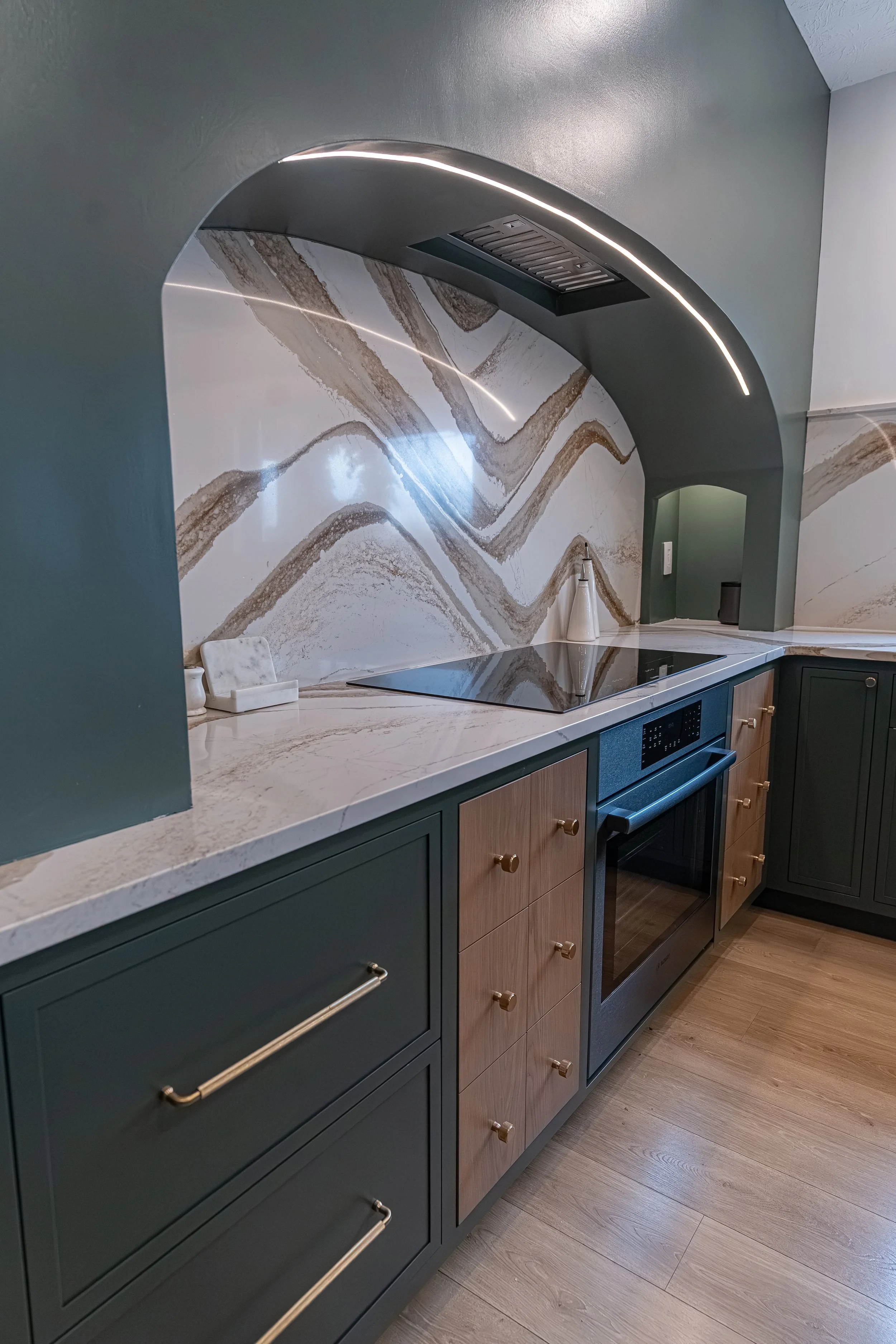 Statement quartz slab backsplash framed by a curved arch above the cooktop with two-tone cabinets