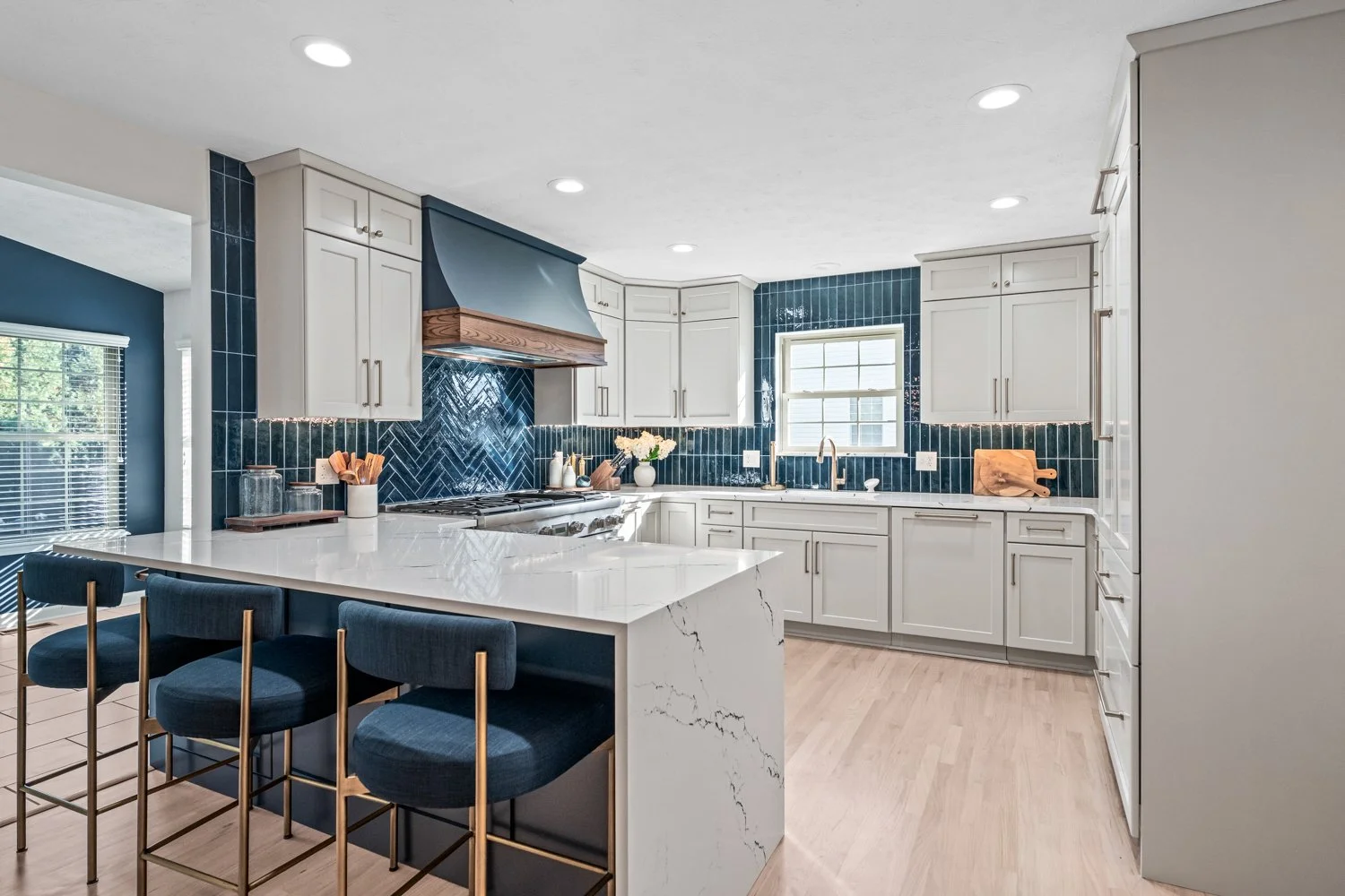 White shaker kitchen with a navy range hood, blue herringbone tile backsplash, and a quartz waterfall peninsula in a Beavercreek, Ohio remodel.
