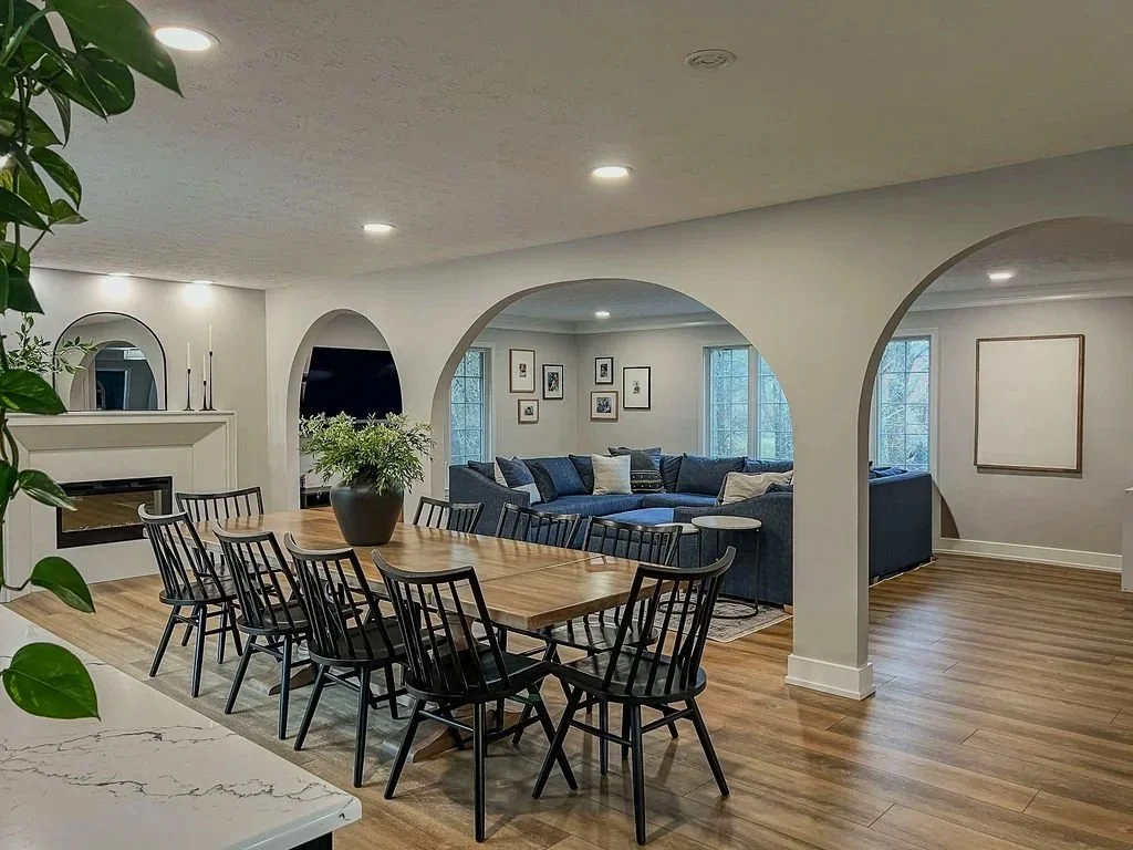 Open dining and living space with a wood dining table, black spindle chairs, and a blue sectional beneath arched doorways in a Centerville remodel.