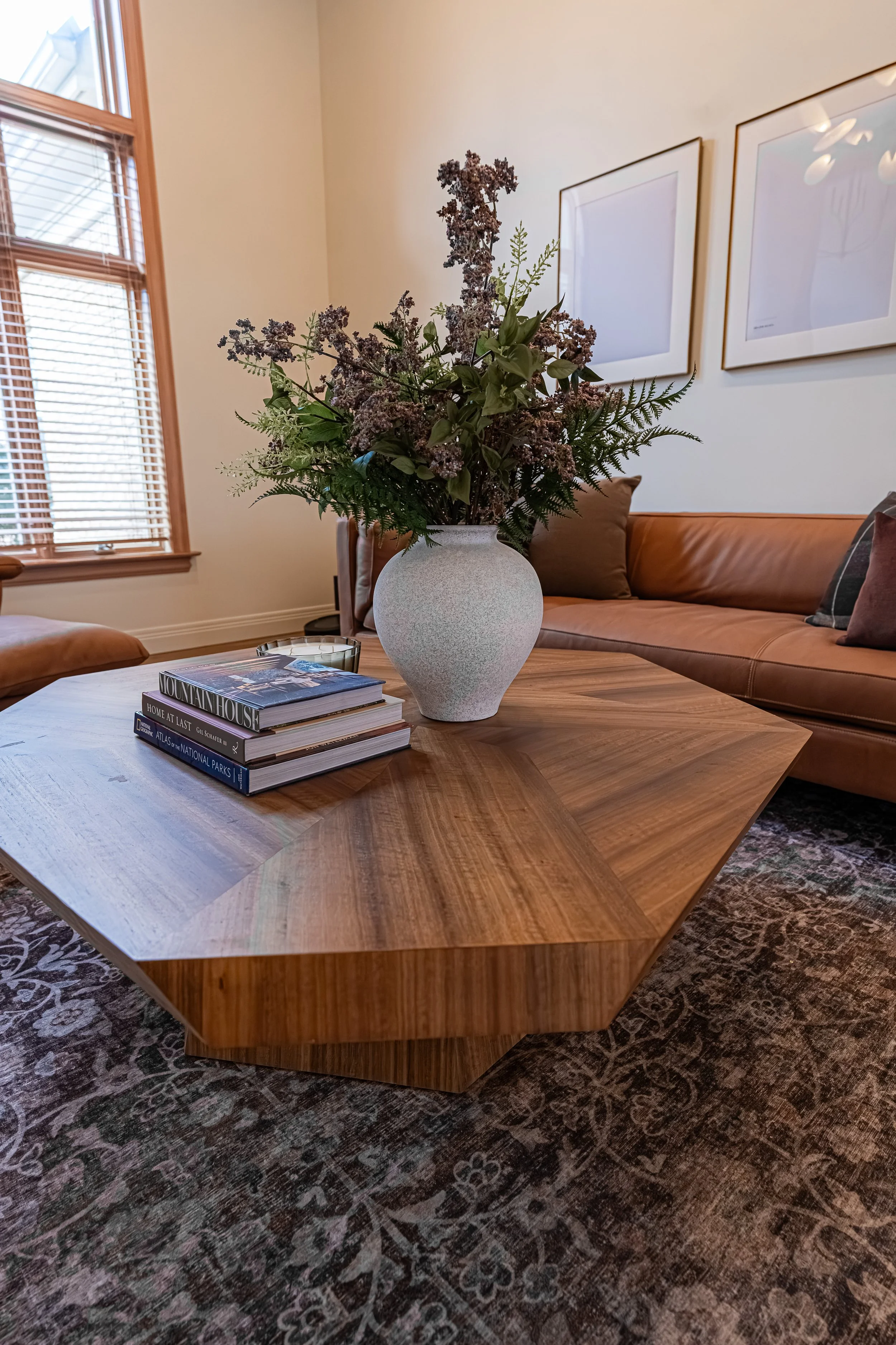 Lounge room with a large hexagonal wood coffee table styled with dried florals beside a tan leather sofa in a Bellbrook whole-home remodel.