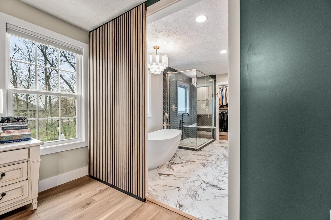 Spa-inspired master bathroom with a freestanding volcanic-stone soaking tub, wood slat accent wall, chandelier, and marble flooring in Xenia, Ohio