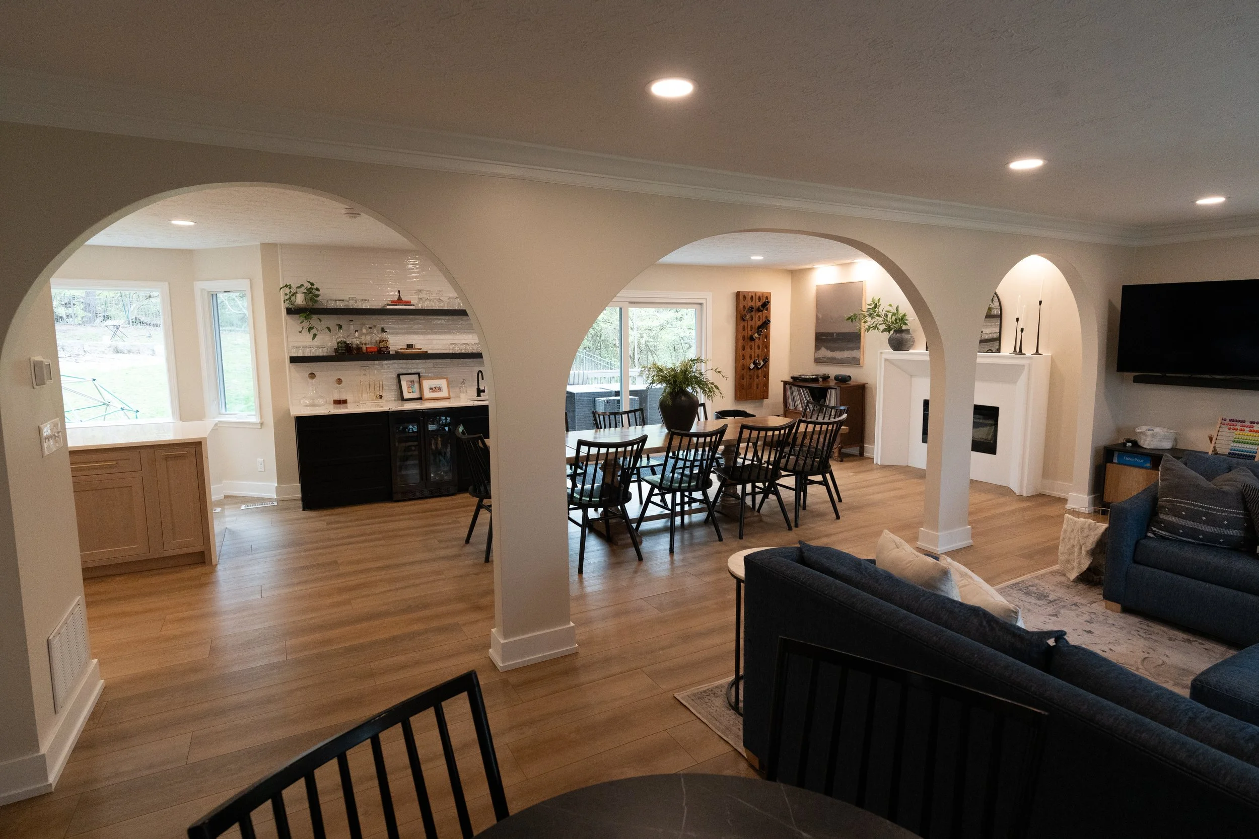 Open-concept dining area with black spindle chairs framed by a custom arched entry, opening to the kitchen and living room in a Centerville whole-home remodel.