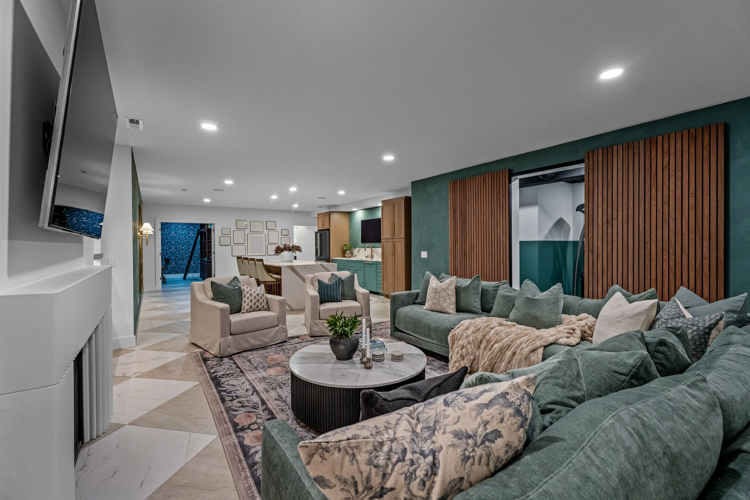 Open-concept finished basement in Centerville, Ohio with a living area, slat-wall feature, and kitchen beyond by White Oak Interiors