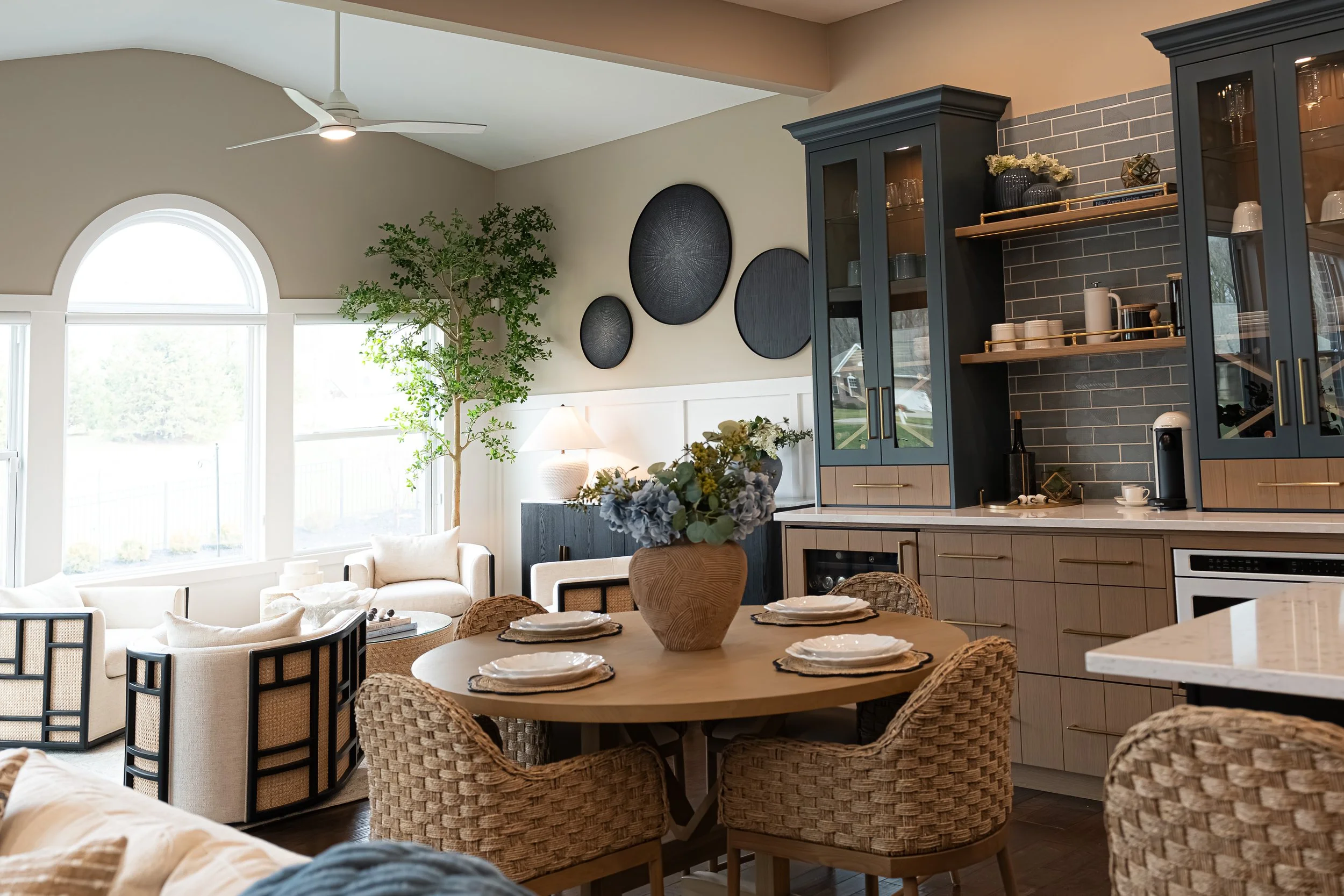 Eat-in dining area with woven chairs open to the living room beside navy cabinetry with open shelving in a Centerville home renovation.