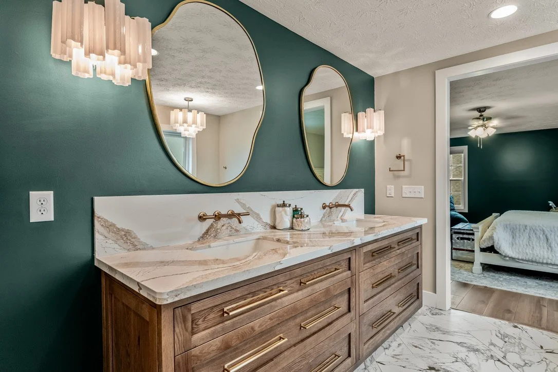 Angled view of a wood double vanity with veined quartz countertop, wall-mounted gold faucets, organic mirrors, and pendant lighting in a Xenia, Ohio master bathroom