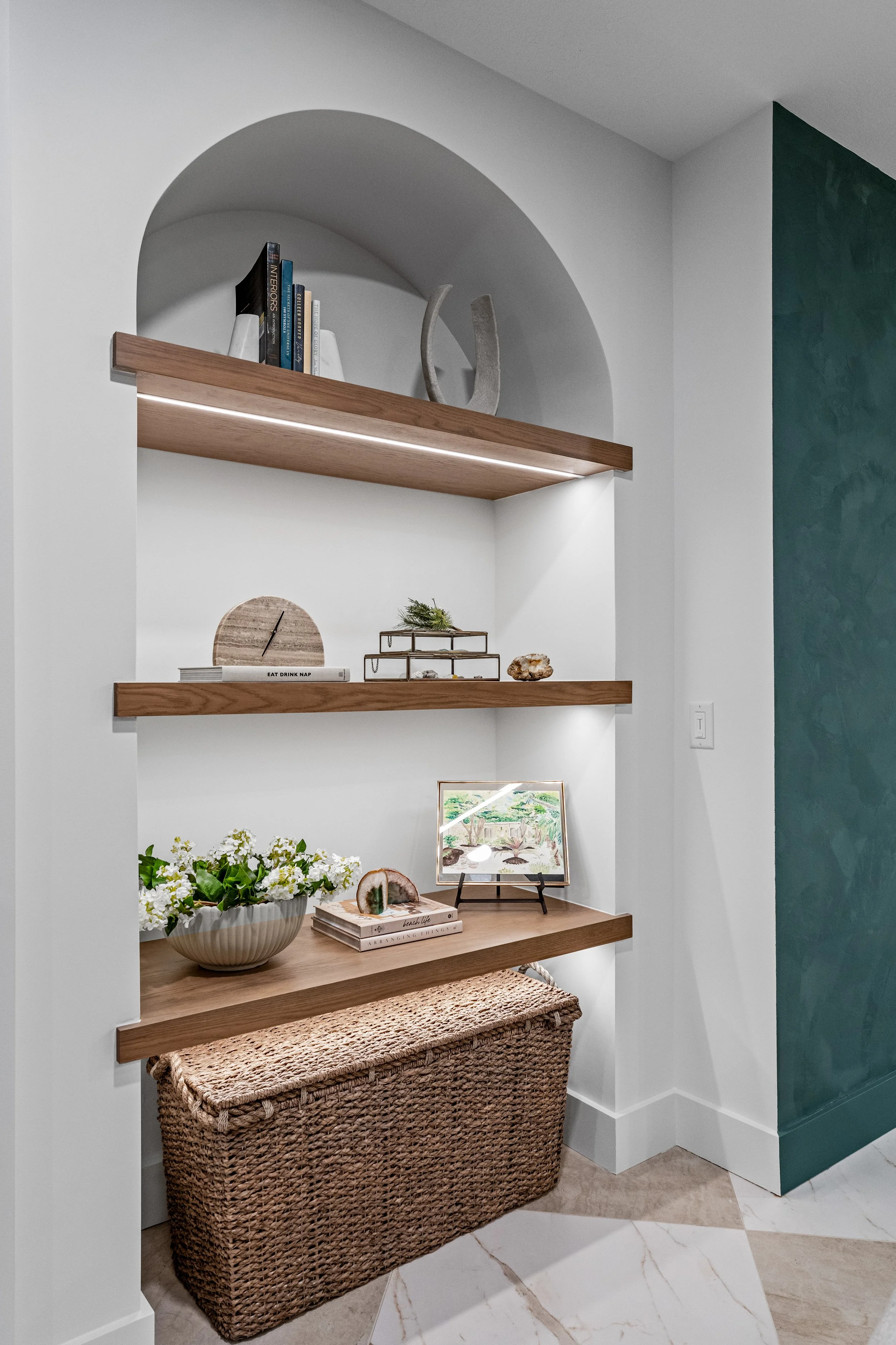 Custom arched built-in with integrated-lighting walnut shelves in a Centerville, Ohio finished basement by White Oak Interiors