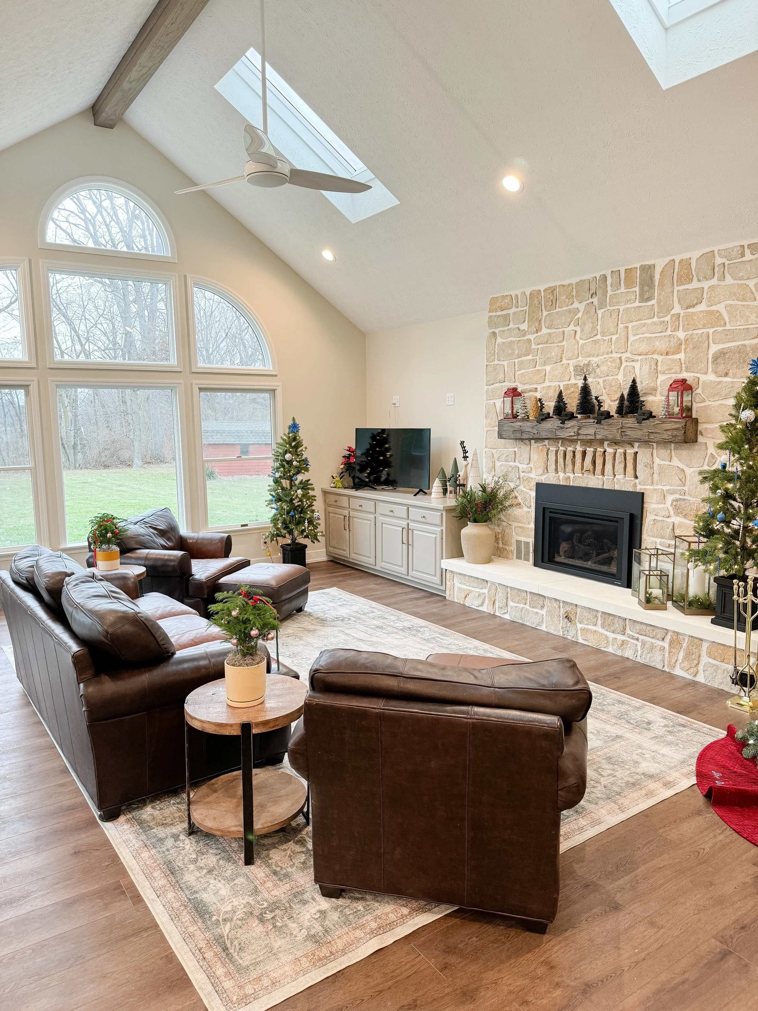 Vaulted living room with a floor-to-ceiling stone fireplace, arched windows, leather sofas, and warm wood flooring