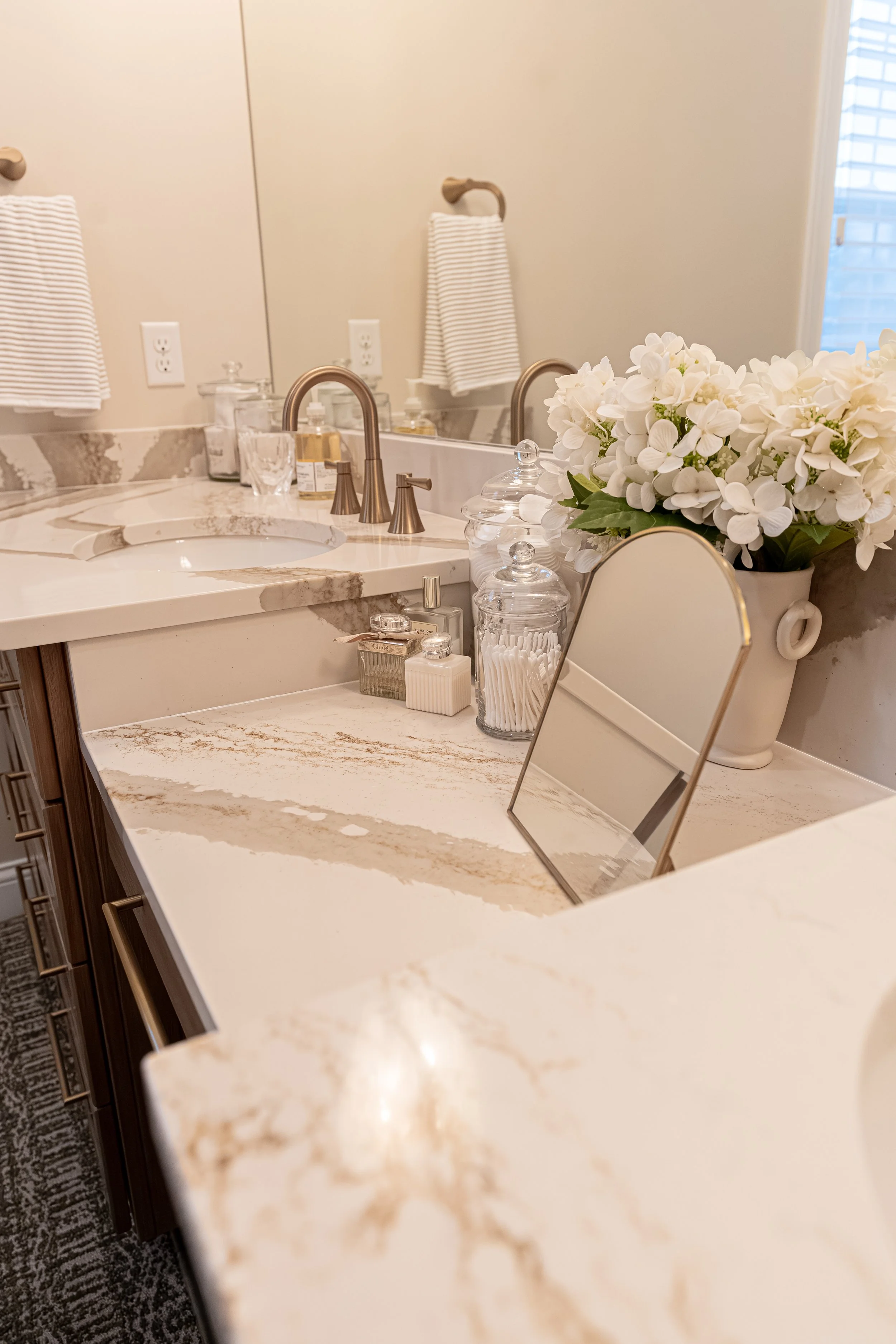 Master bathroom vanity detail with quartz countertop, brushed gold faucet, arched vanity mirror, and styled accessories in an Oakwood, Ohio home