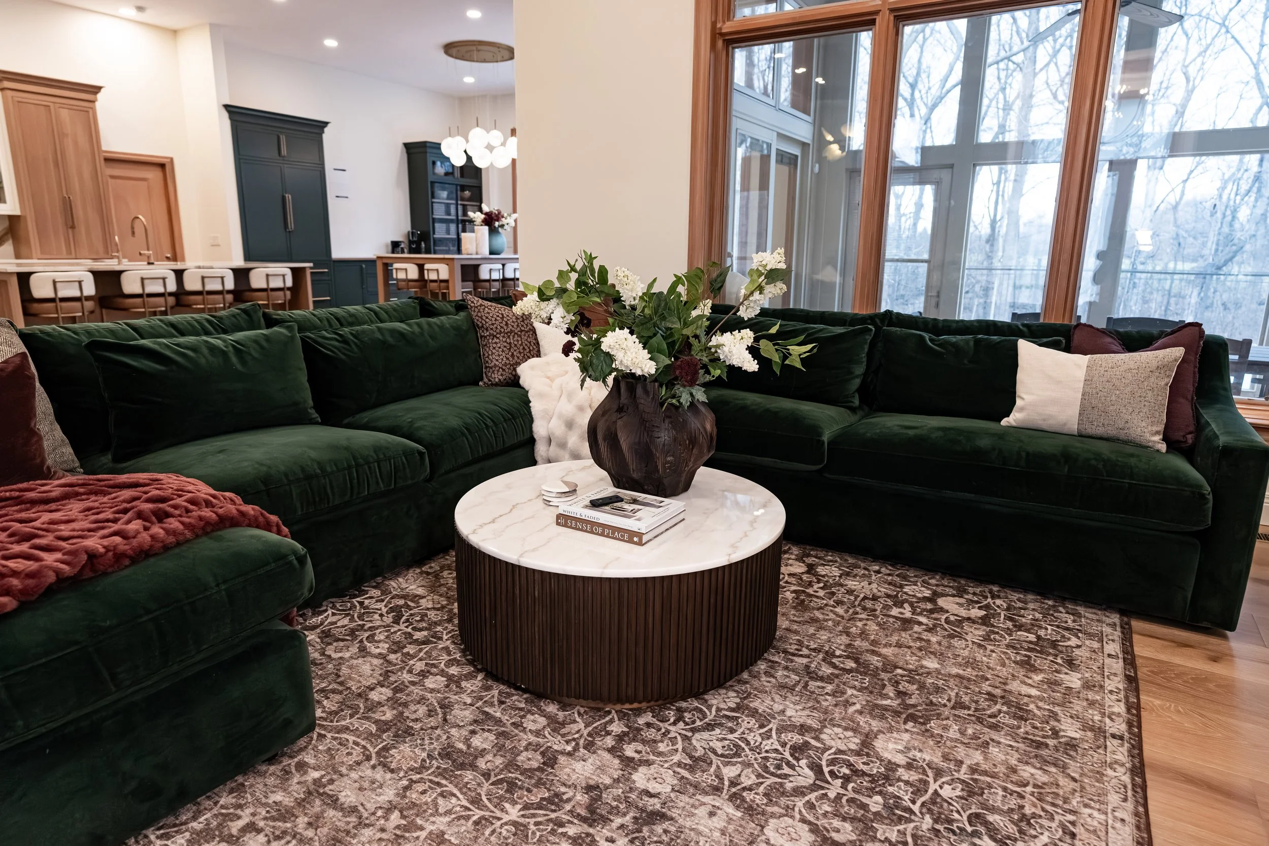 Green velvet sectional and layered styling beneath floor-to-ceiling windows in a Bellbrook, Ohio living room by White Oak Interiors