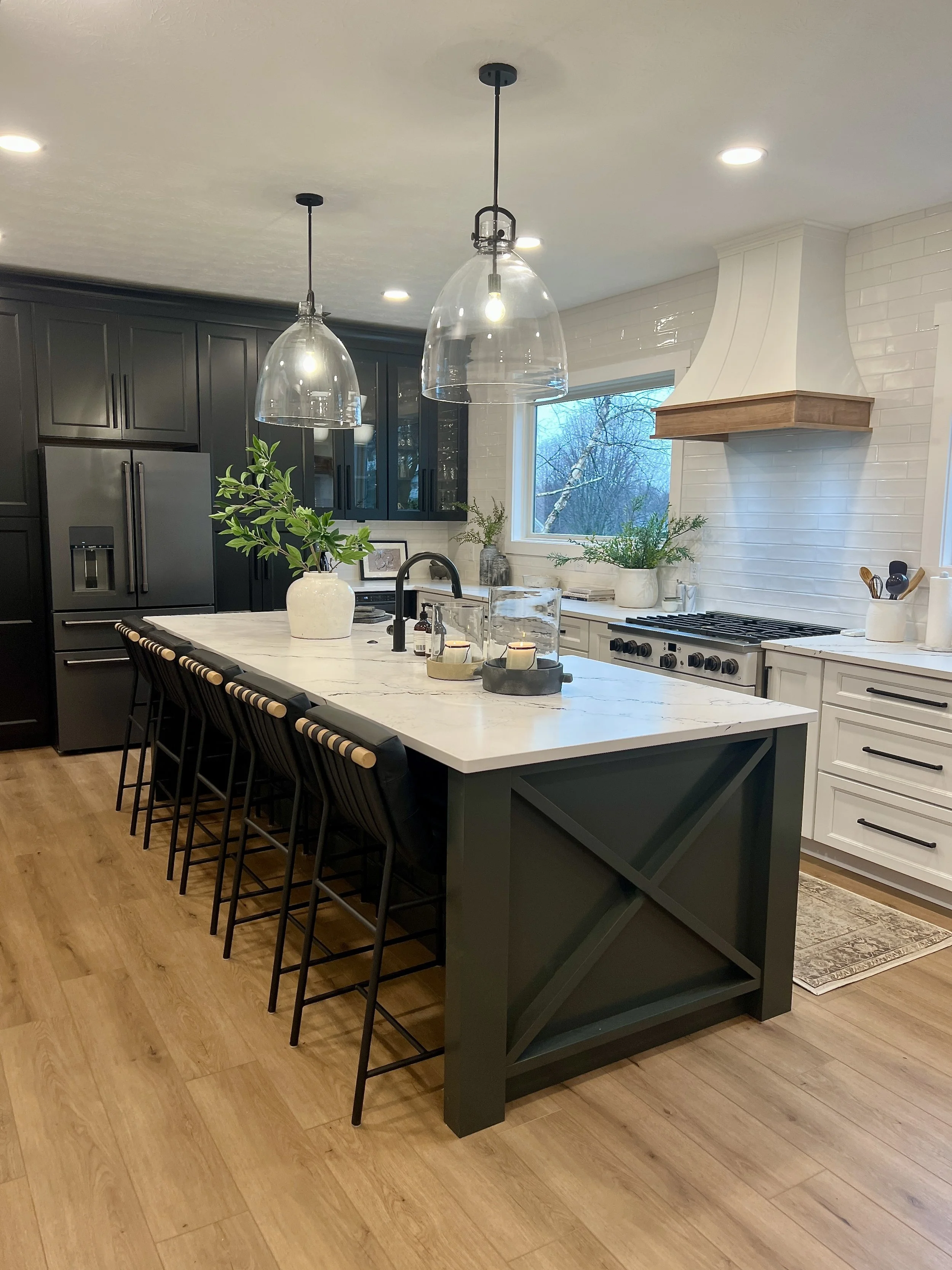 Renovated kitchen with a dark green island featuring an X-panel detail, white quartz countertop, counter stools, and glass pendant lights in a Springboro, Ohio home