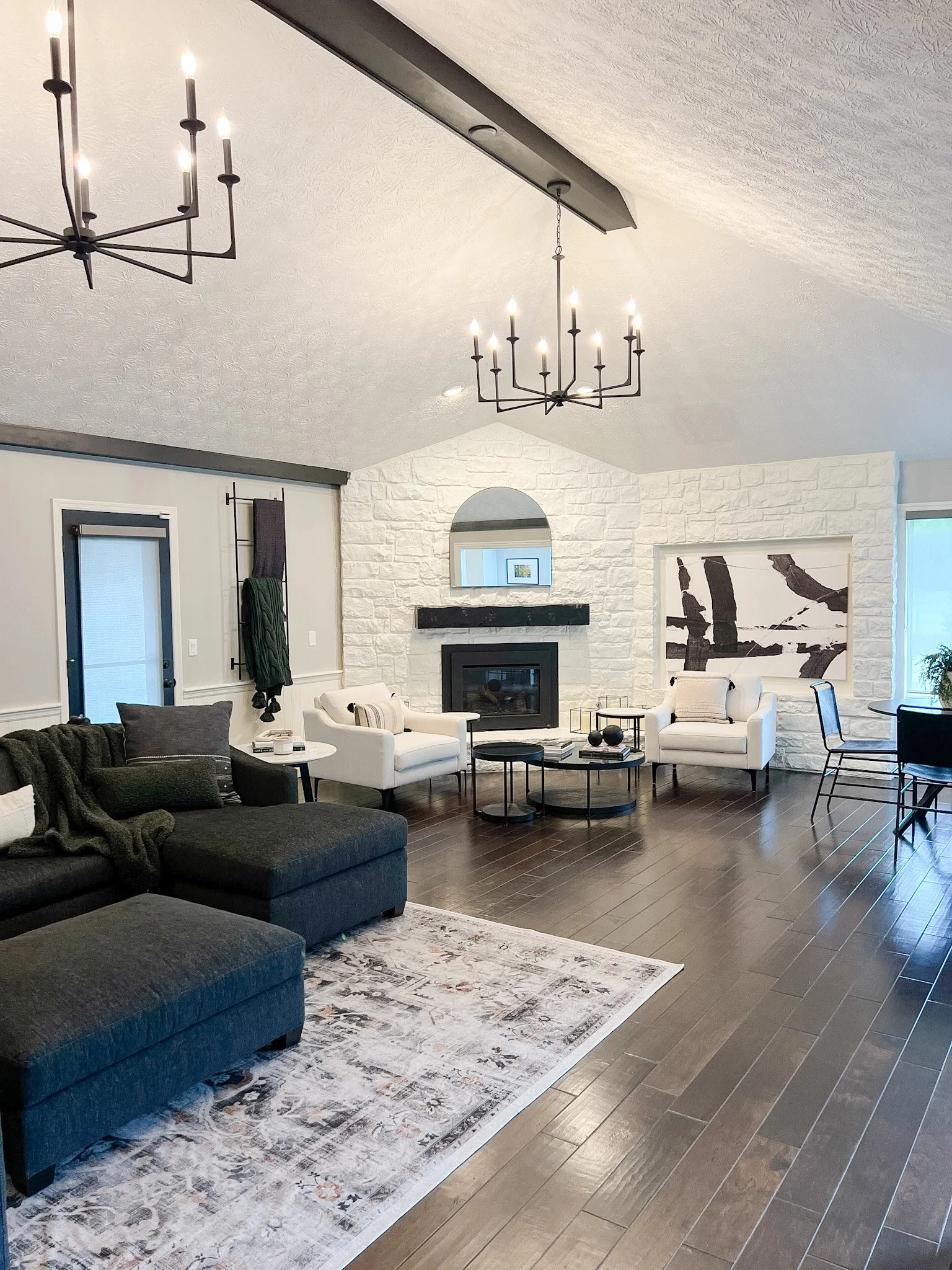 Living room with a floor-to-ceiling white stone fireplace, vaulted beamed ceiling, dual black chandeliers, and a gray sectional in a Centerville, Ohio home