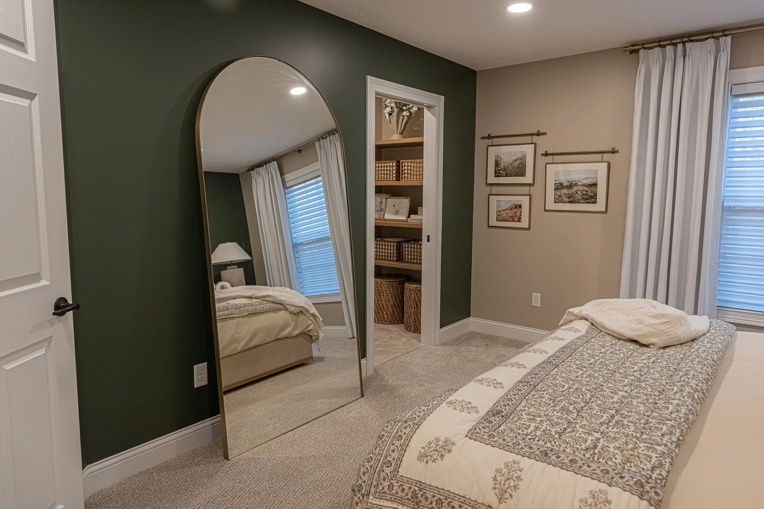 Guest bedroom with a green accent wall, large arched floor mirror, framed gallery art, and warm neutral bedding in an Oakwood, Ohio home