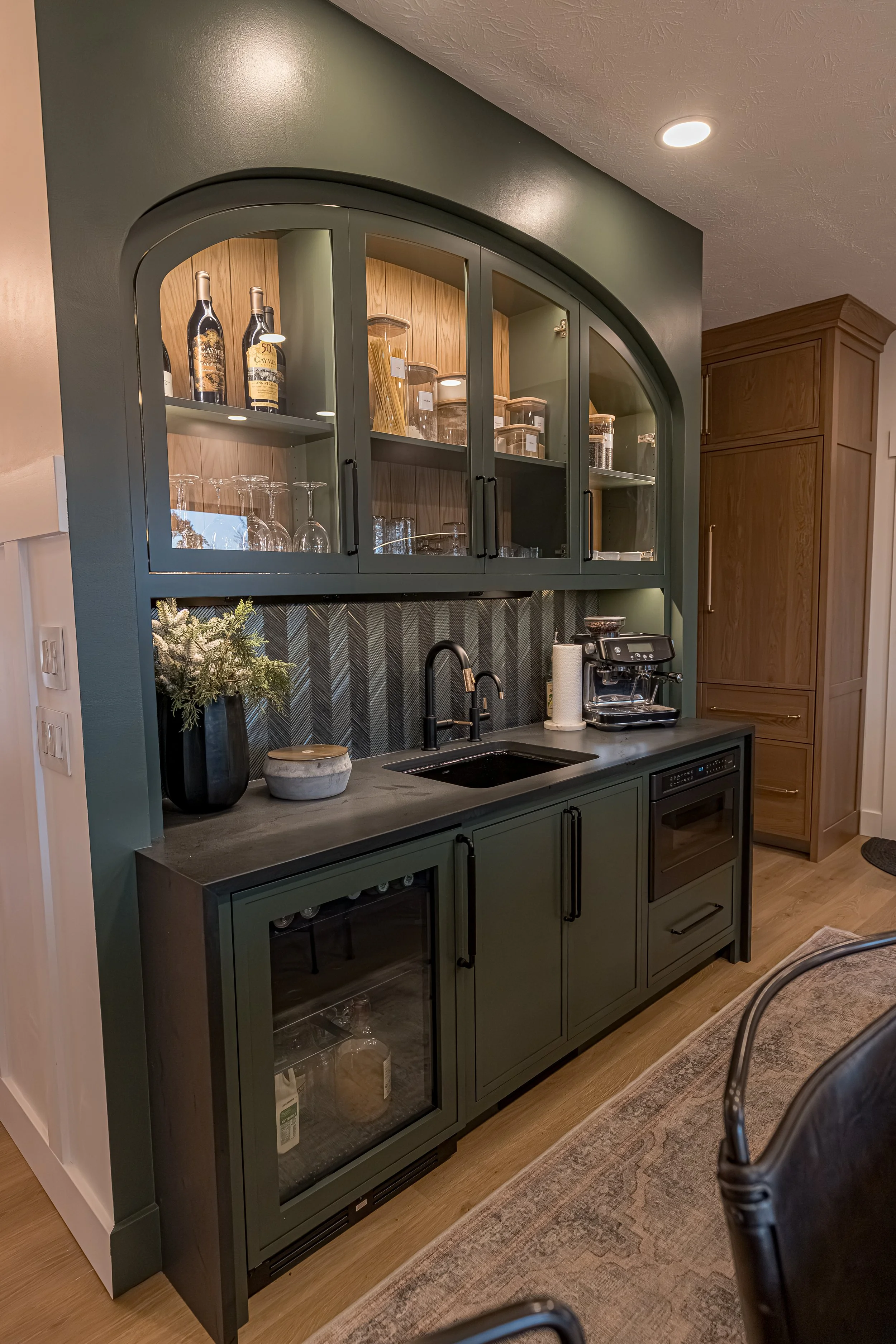 Built-in coffee and wine bar with arched glass cabinets and herringbone tile backsplash