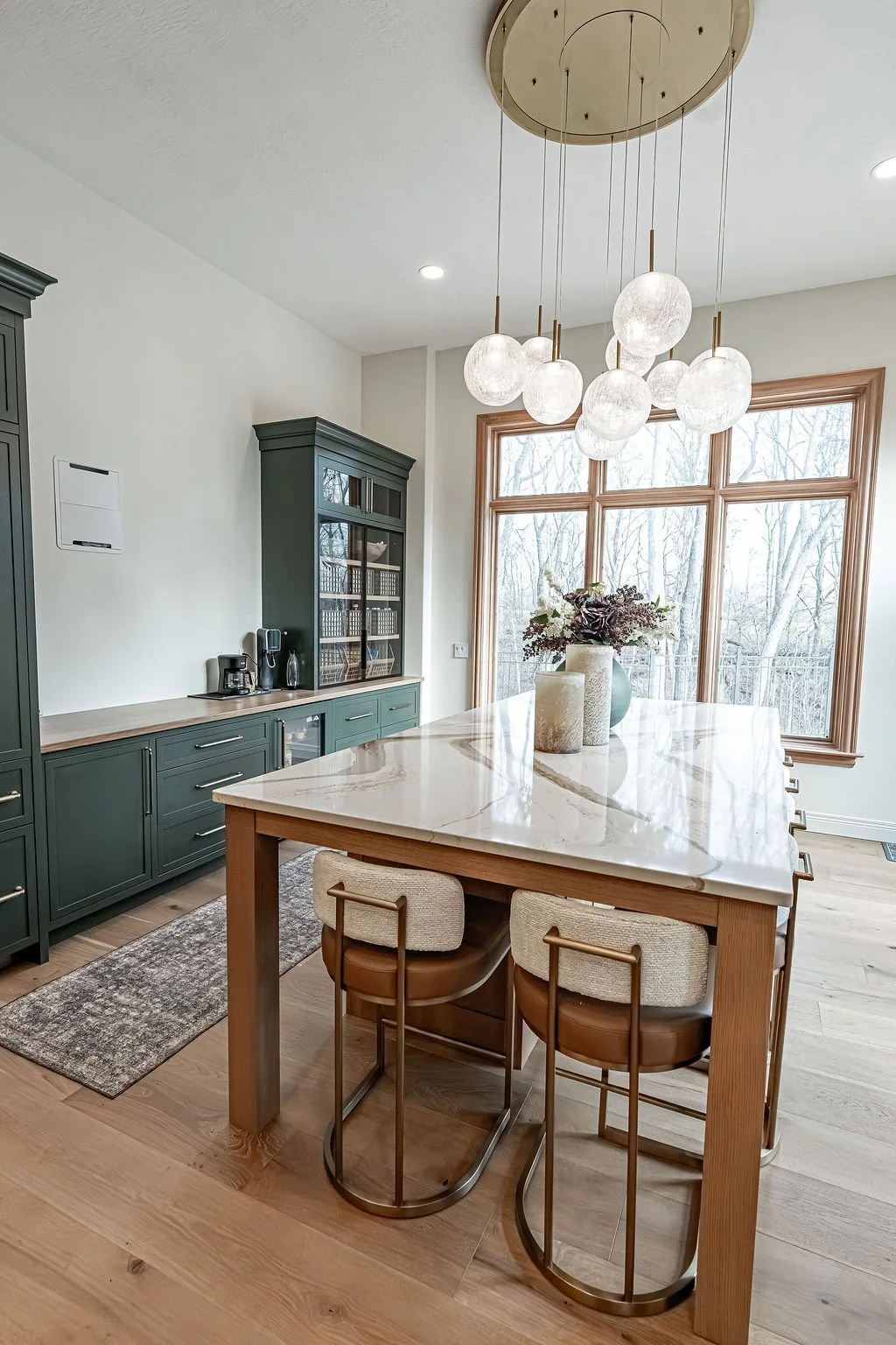 Kitchen with a large marble island, green cabinets, and a pendant light fixture with multiple glass orbs.