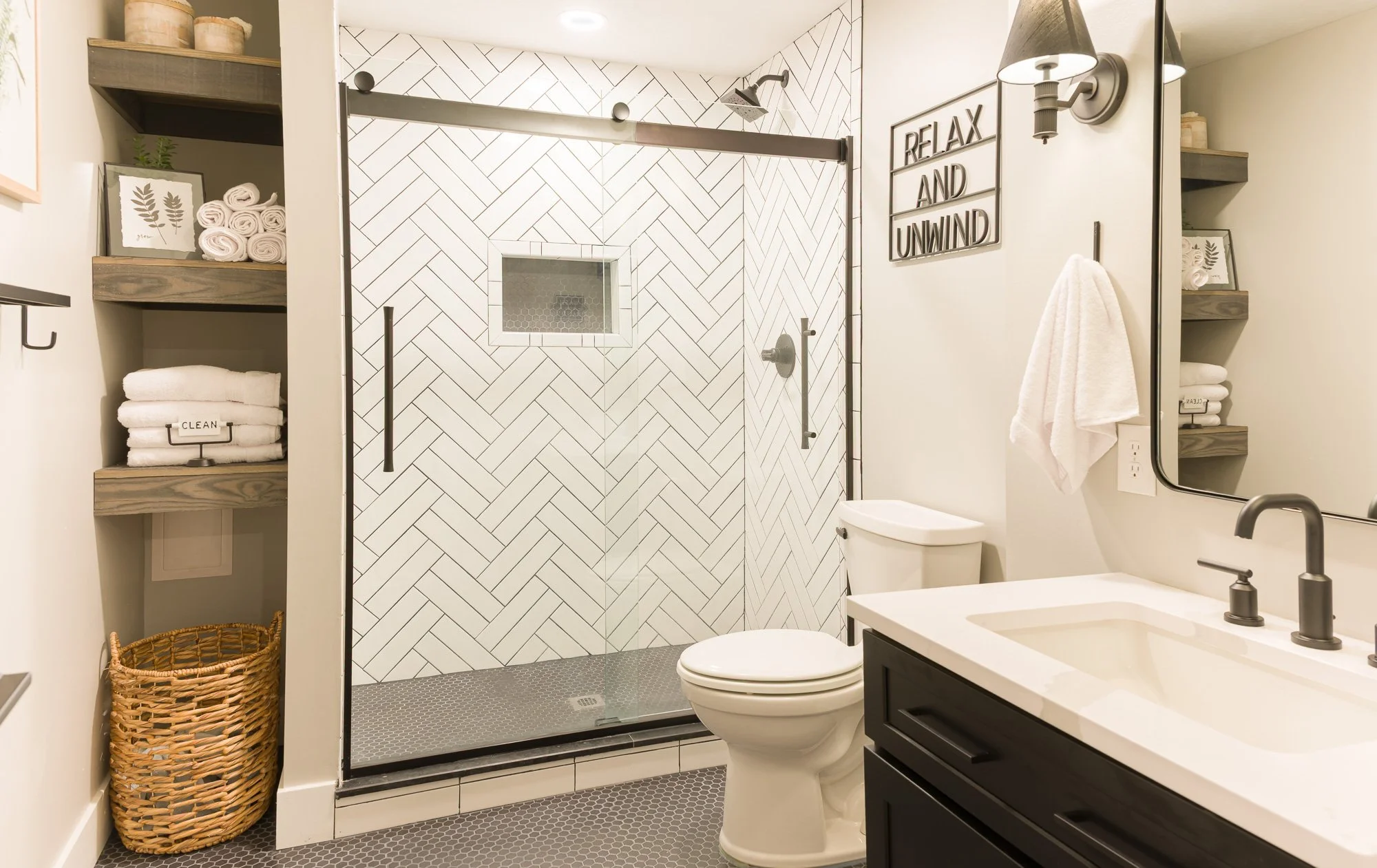 Basement full bath with white herringbone shower tile, charcoal penny floor, and black vanity in Beavercreek, Ohio