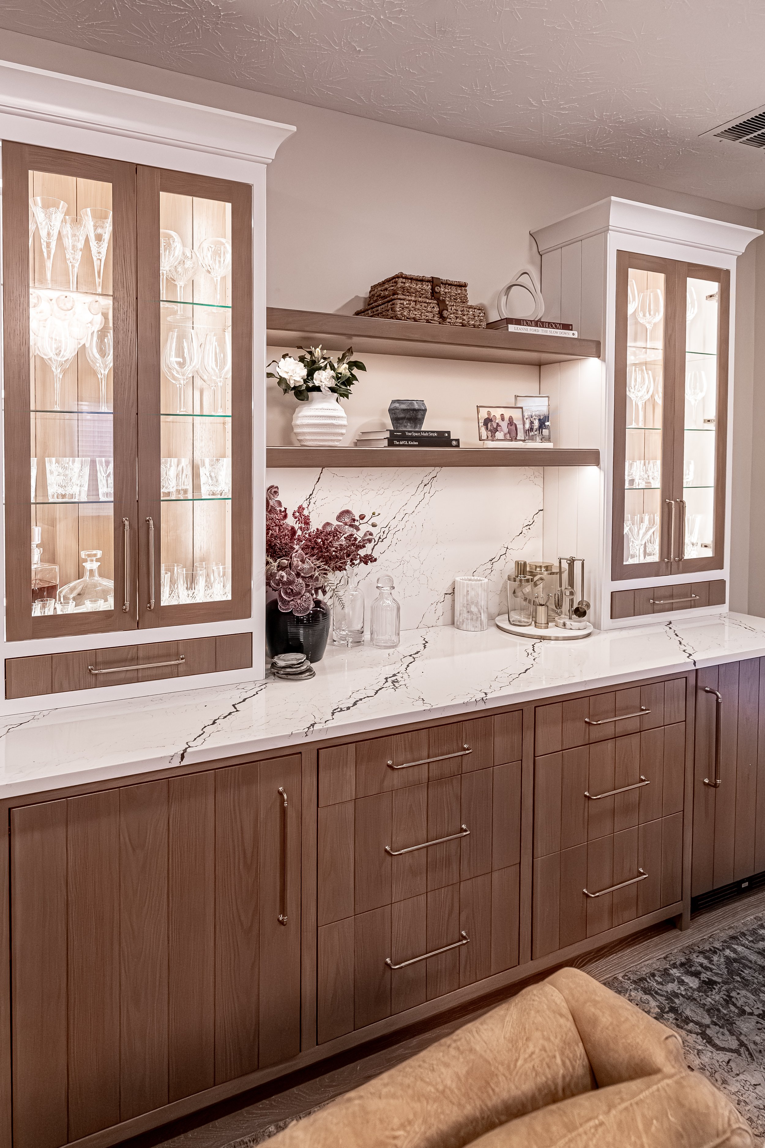 Styled white oak wine bar with illuminated glass-front cabinets, quartz waterfall countertop and backsplash, and open shelving in an Oakwood, Ohio home