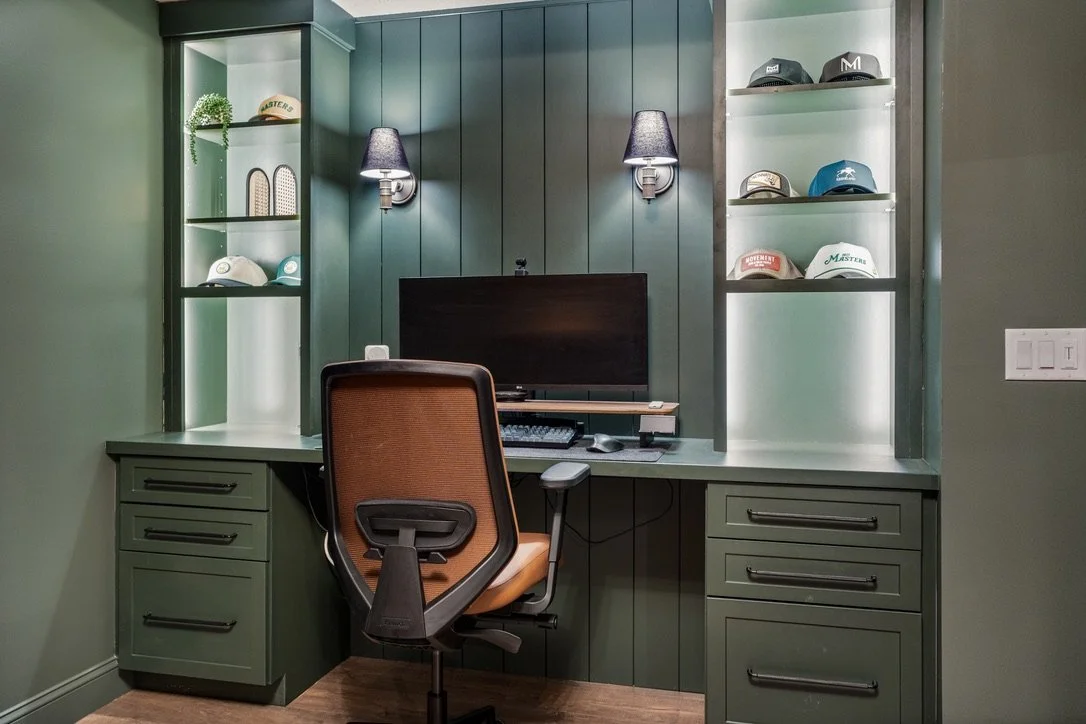 Built-in basement home office with green paneled walls, display shelving, and brass sconces in a Brookville, Ohio basement renovation.