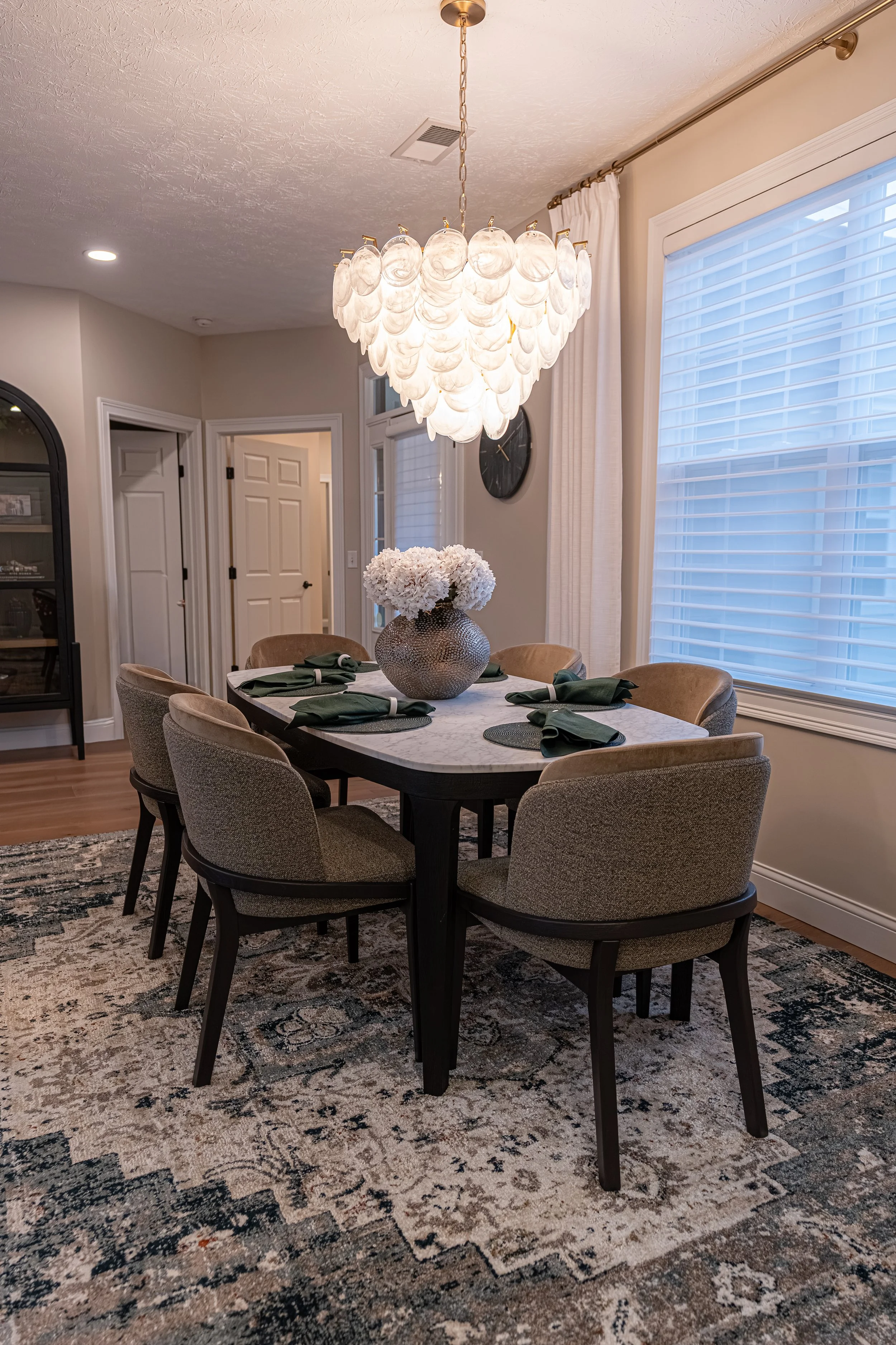 Renovated dining room with an upholstered table and chairs, sculptural fogged-glass chandelier, layered area rug, and soft natural light in Oakwood, Ohio