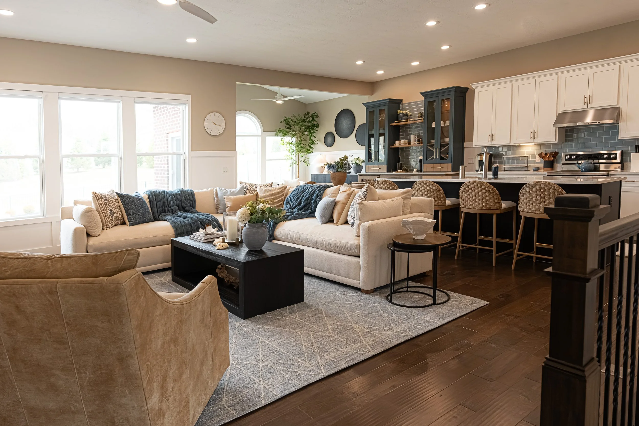 Open living room with a cream sectional, patterned rug, and black coffee table flowing to the navy-and-white kitchen in a Centerville home renovation.