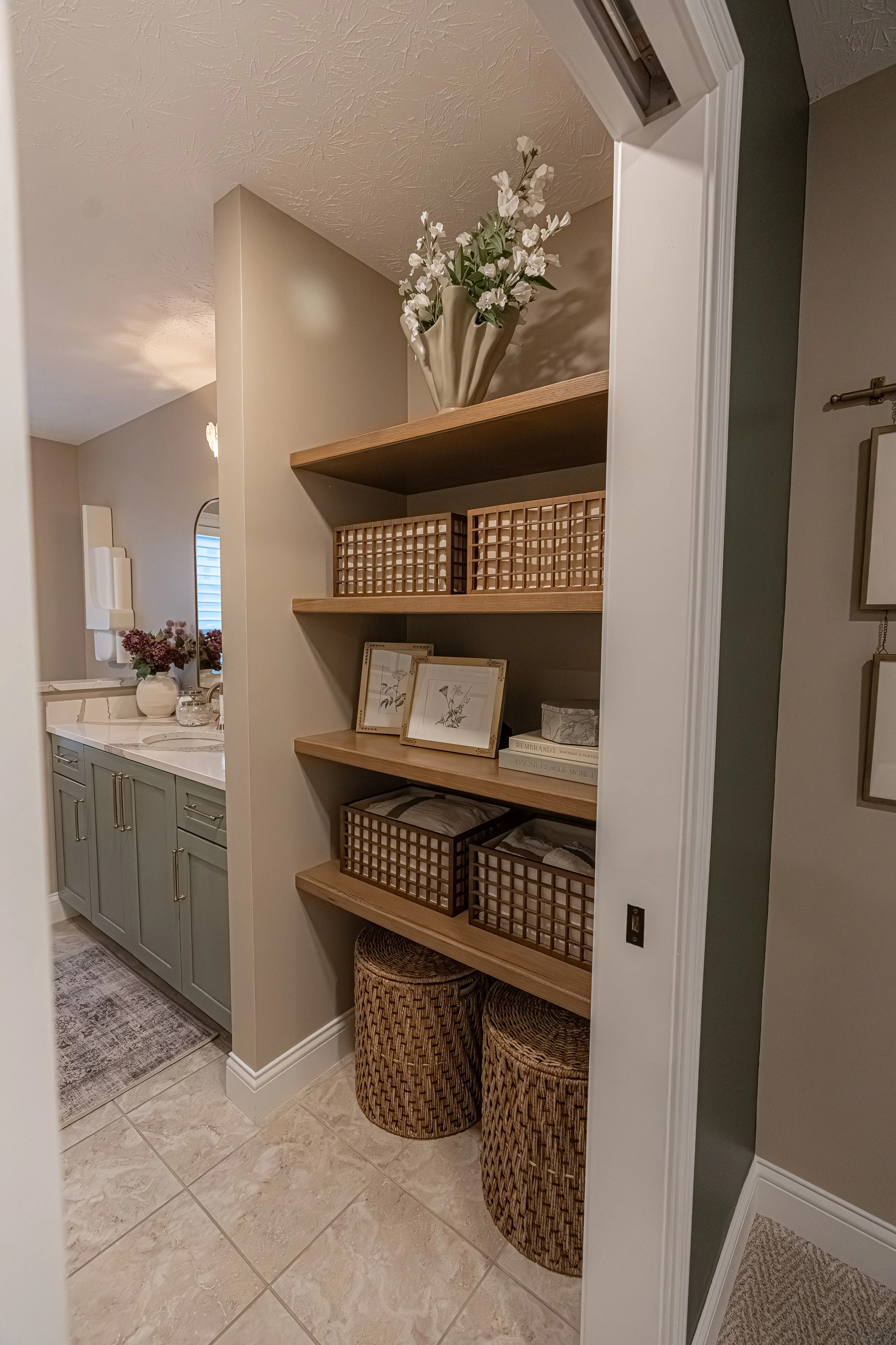 Guest bathroom with built-in wood open shelving, woven storage baskets, green vanity, and styled decor opening to a tiled bath in an Oakwood, Ohio home