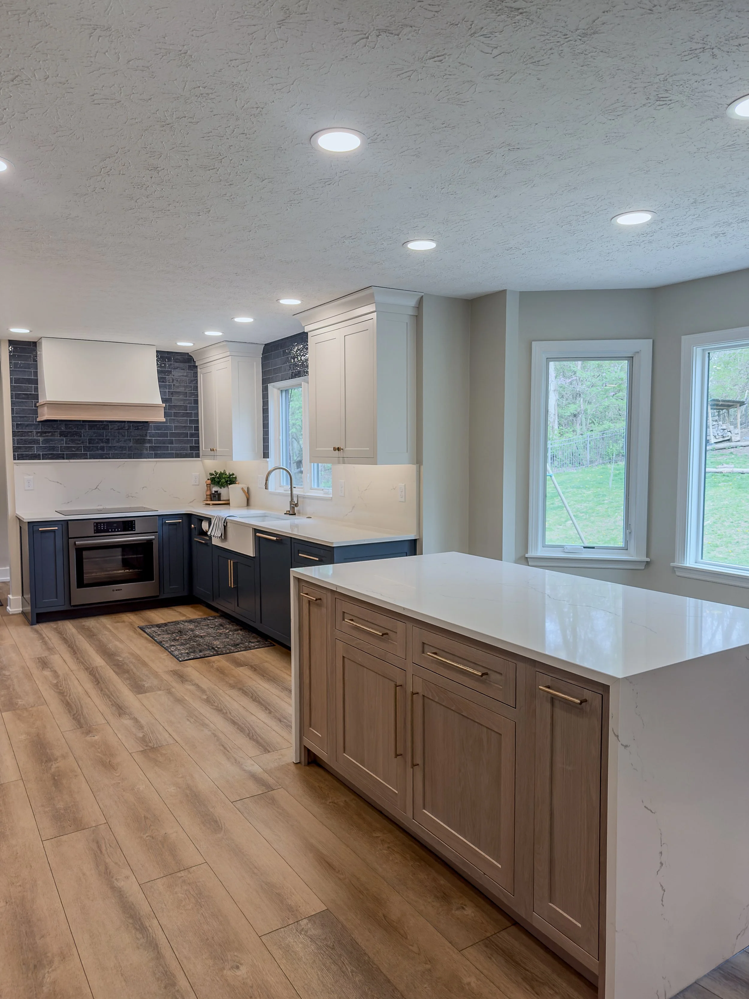 Imperial Woods kitchen remodel in Dayton, Ohio with navy and white cabinetry, marble island, brass hardware, and navy tile range wall by White Oak Interiors