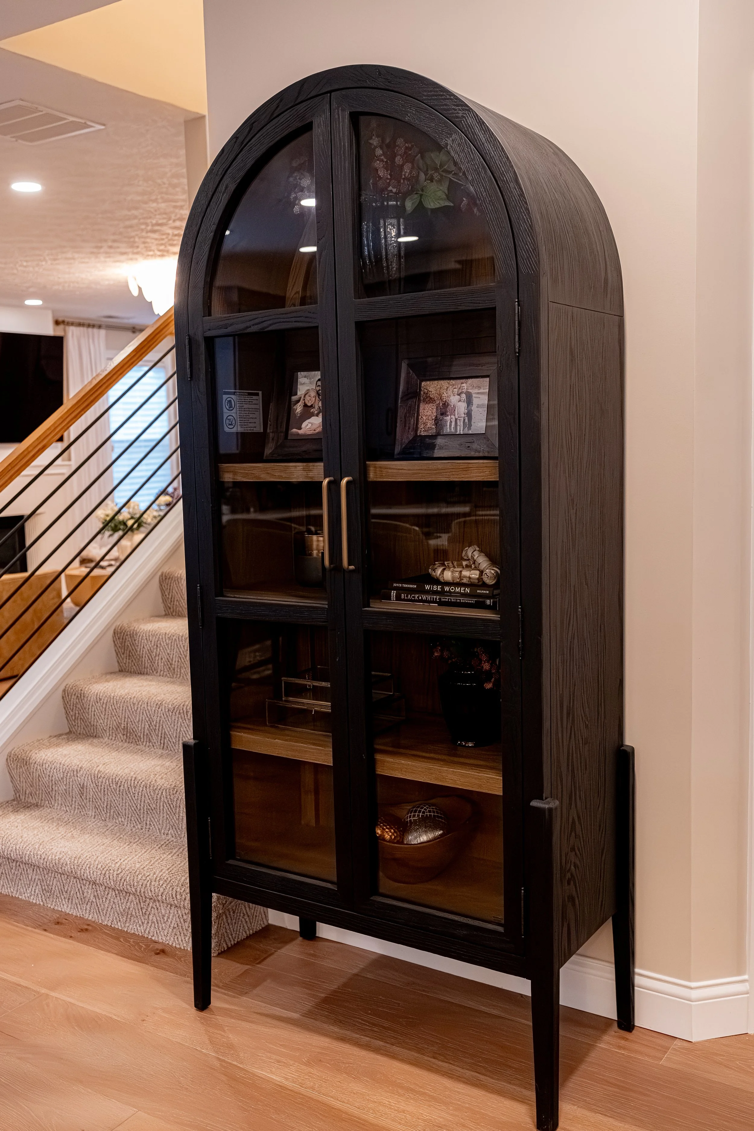 Renovated staircase with a custom horizontal metal-and-wood railing and new carpet runner, beside a black arched display cabinet in an Oakwood, Ohio home