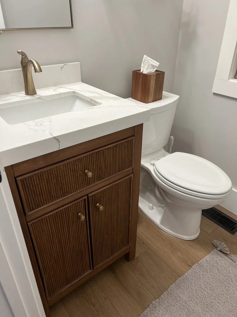 Renovated half bath with a reeded wood vanity, veined quartz countertop, gold faucet and hardware, and light wood flooring in a Springboro, Ohio home