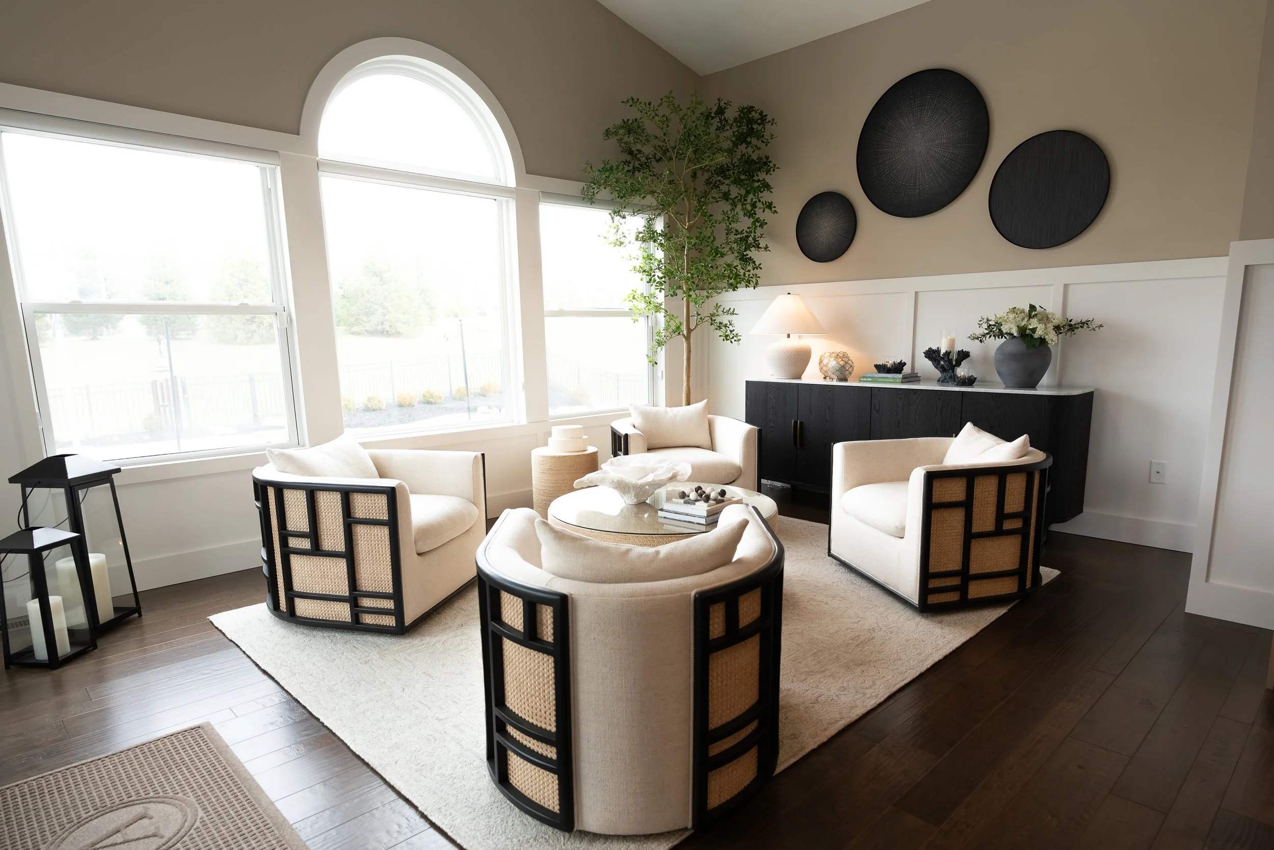 Formal sitting room with cream swivel and cane chairs around a woven drum table beneath an arched window in a Centerville home renovation.