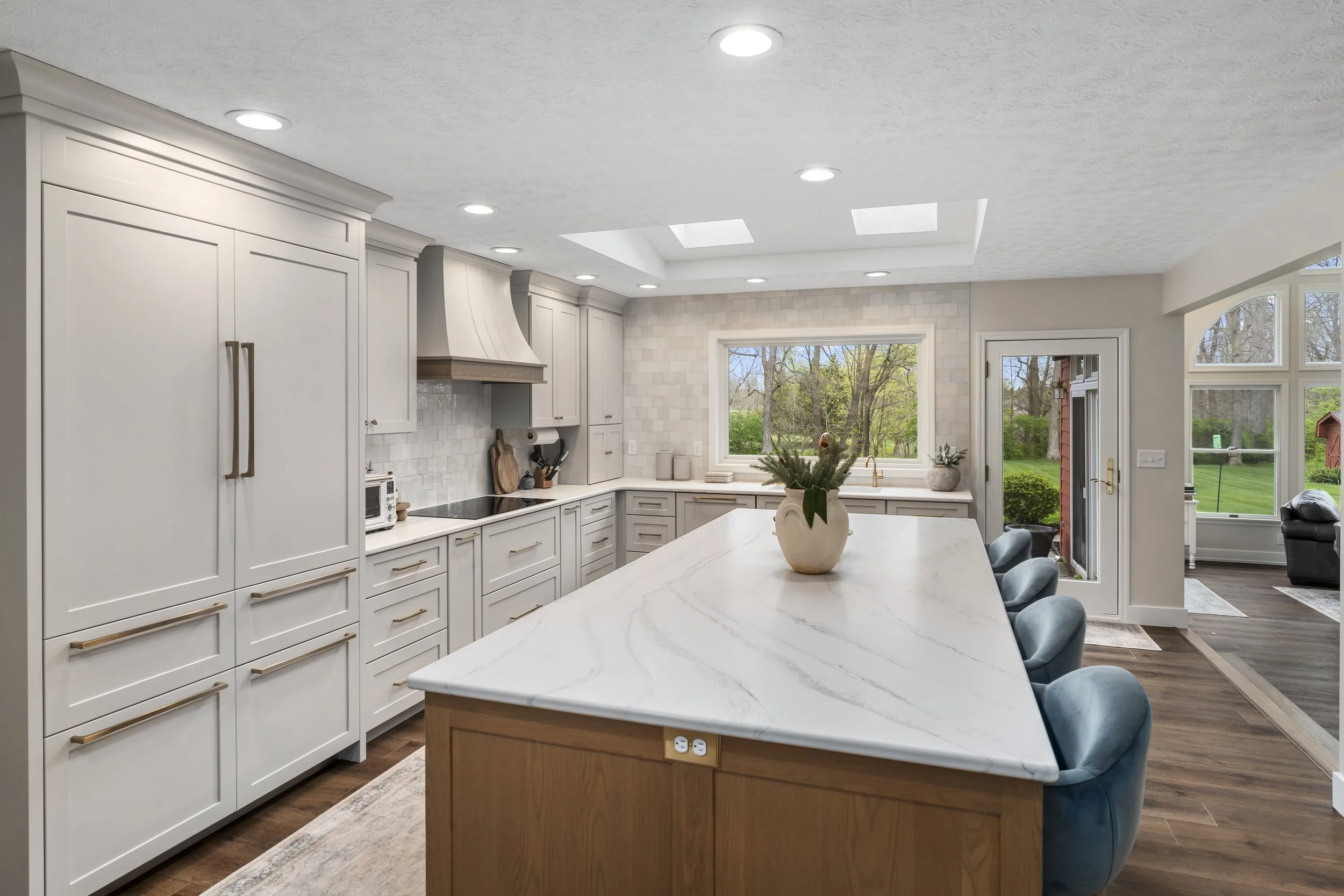 Open kitchen layout with light wood island, white quartz countertops, custom hood, integrated panel refrigerator, and access to the backyard"