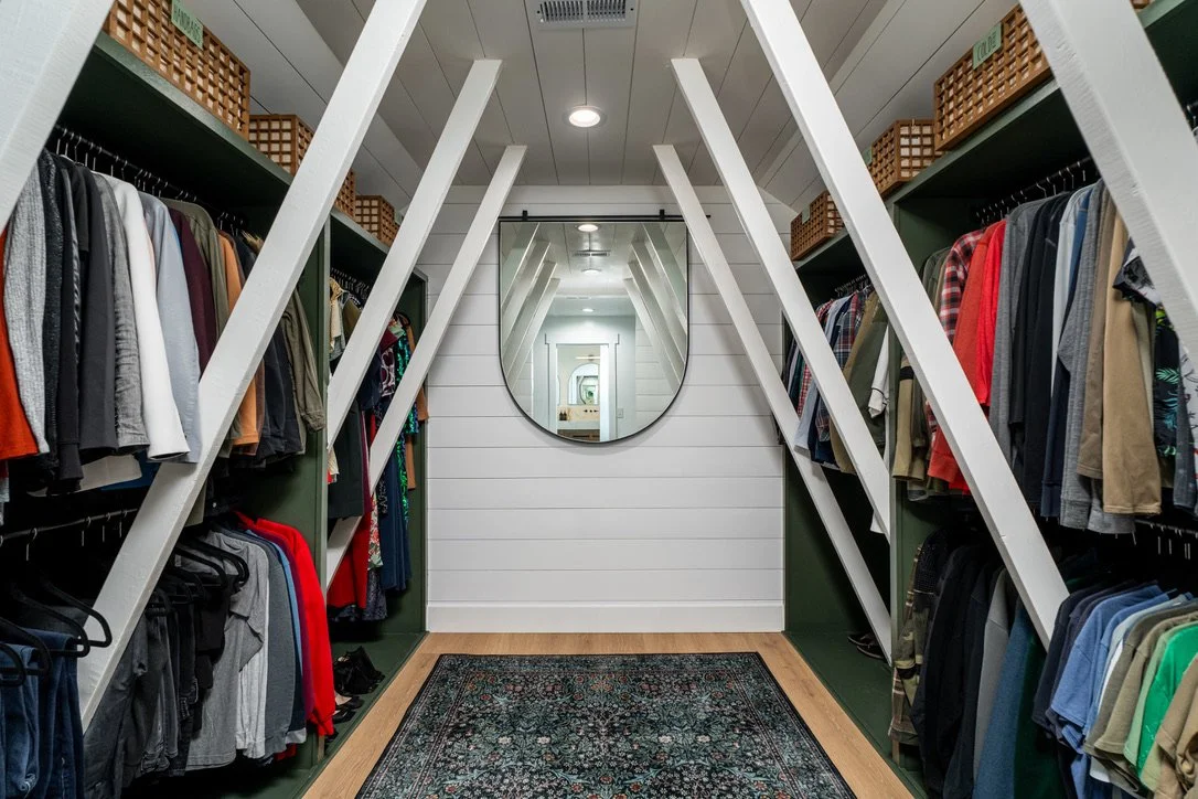 Custom walk-in master closet with sloped shiplap ceiling, green built-in shelving, woven storage baskets, an arched mirror, and a patterned area rug