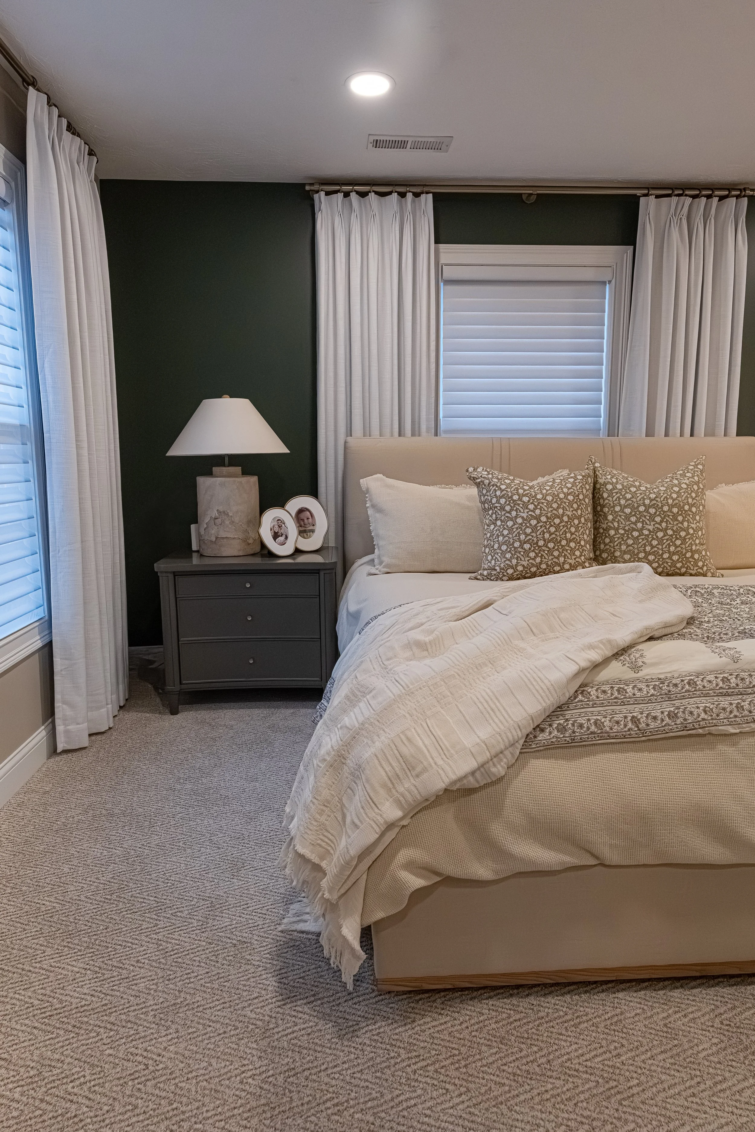 Cozy guest bedroom with a deep green wall, layered neutral and patterned bedding, a wood nightstand, and soft natural light in an Oakwood, Ohio renovation