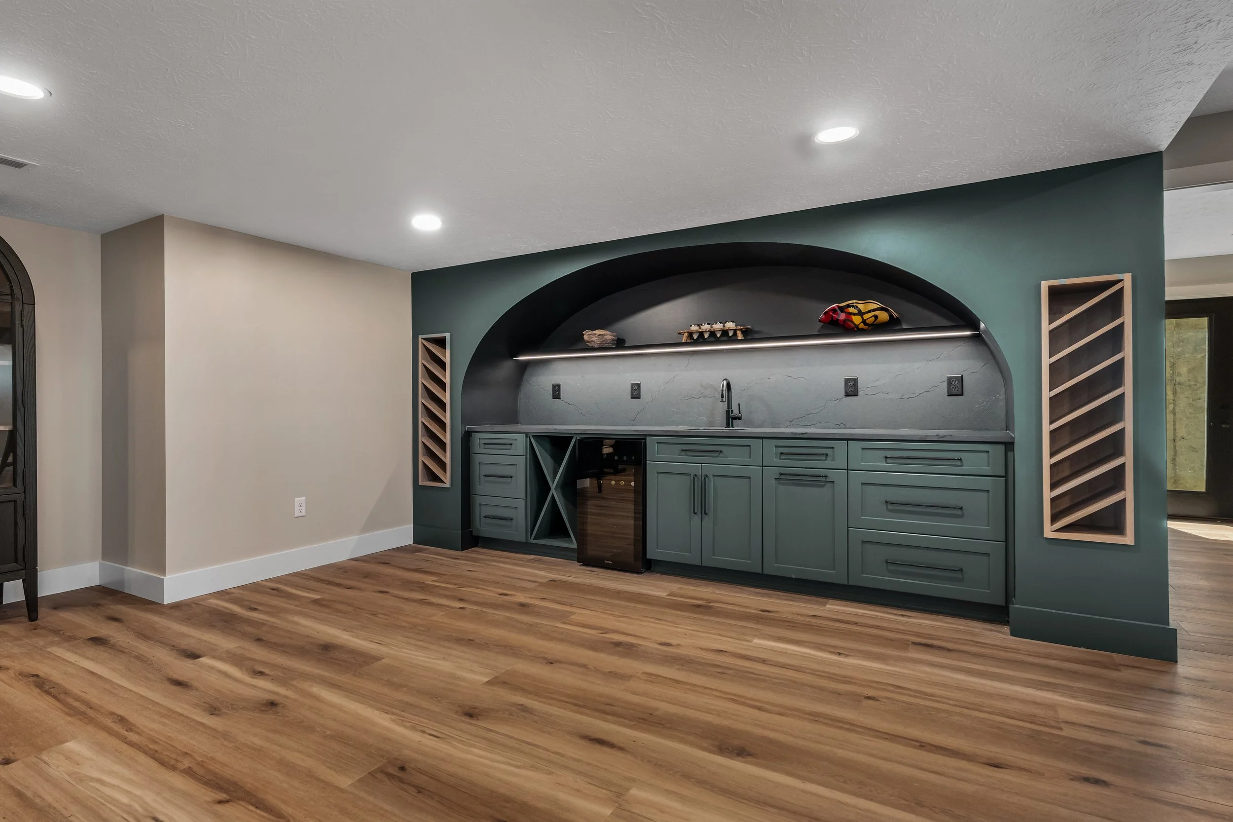 Custom arched wet bar with green cabinetry, marble backsplash, and angled wood wine racks in a Brehm basement renovation by White Oak Interiors